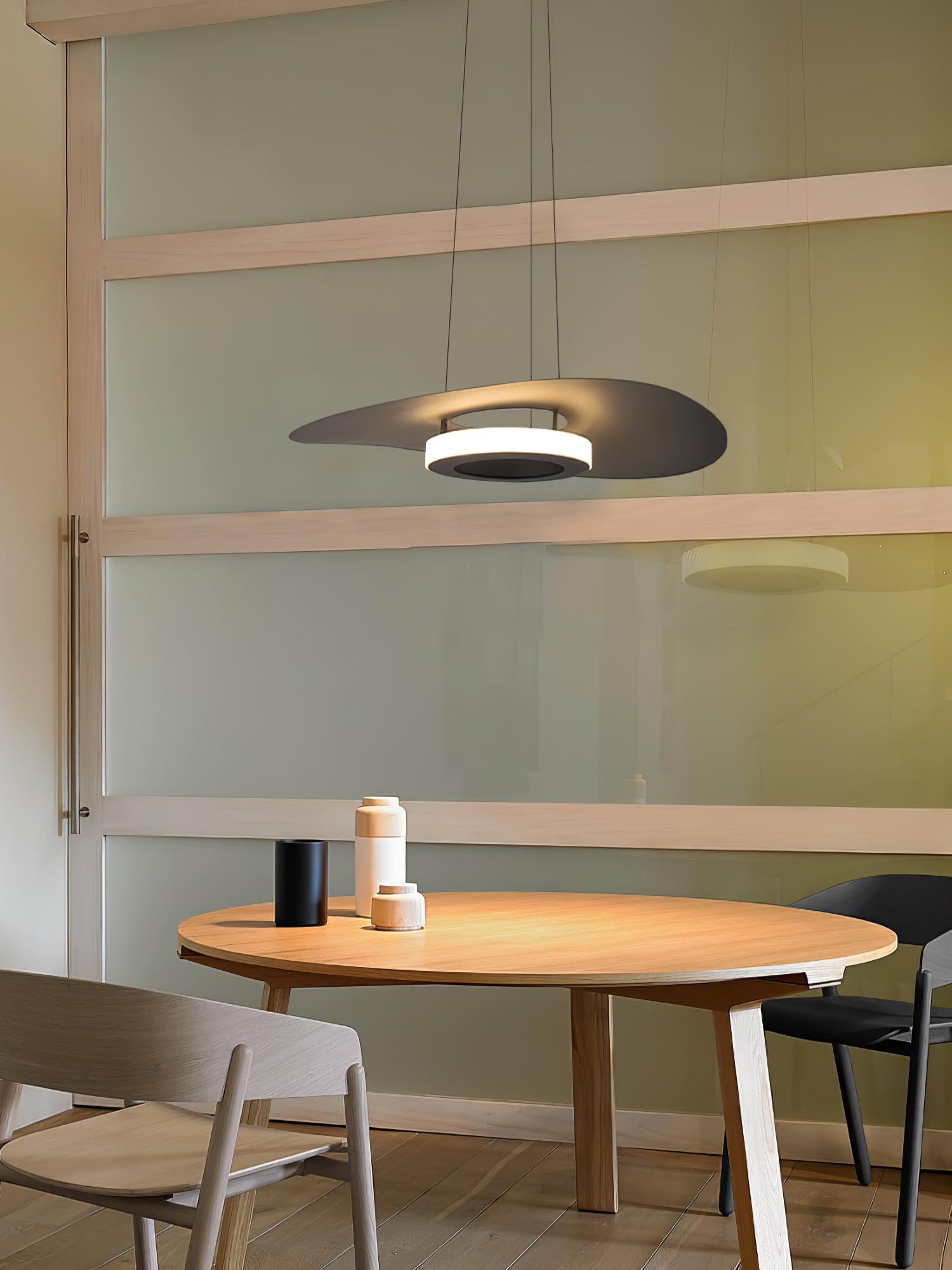 Wider dining view of dark disc pendant over round wood table beside green partition and pale chair