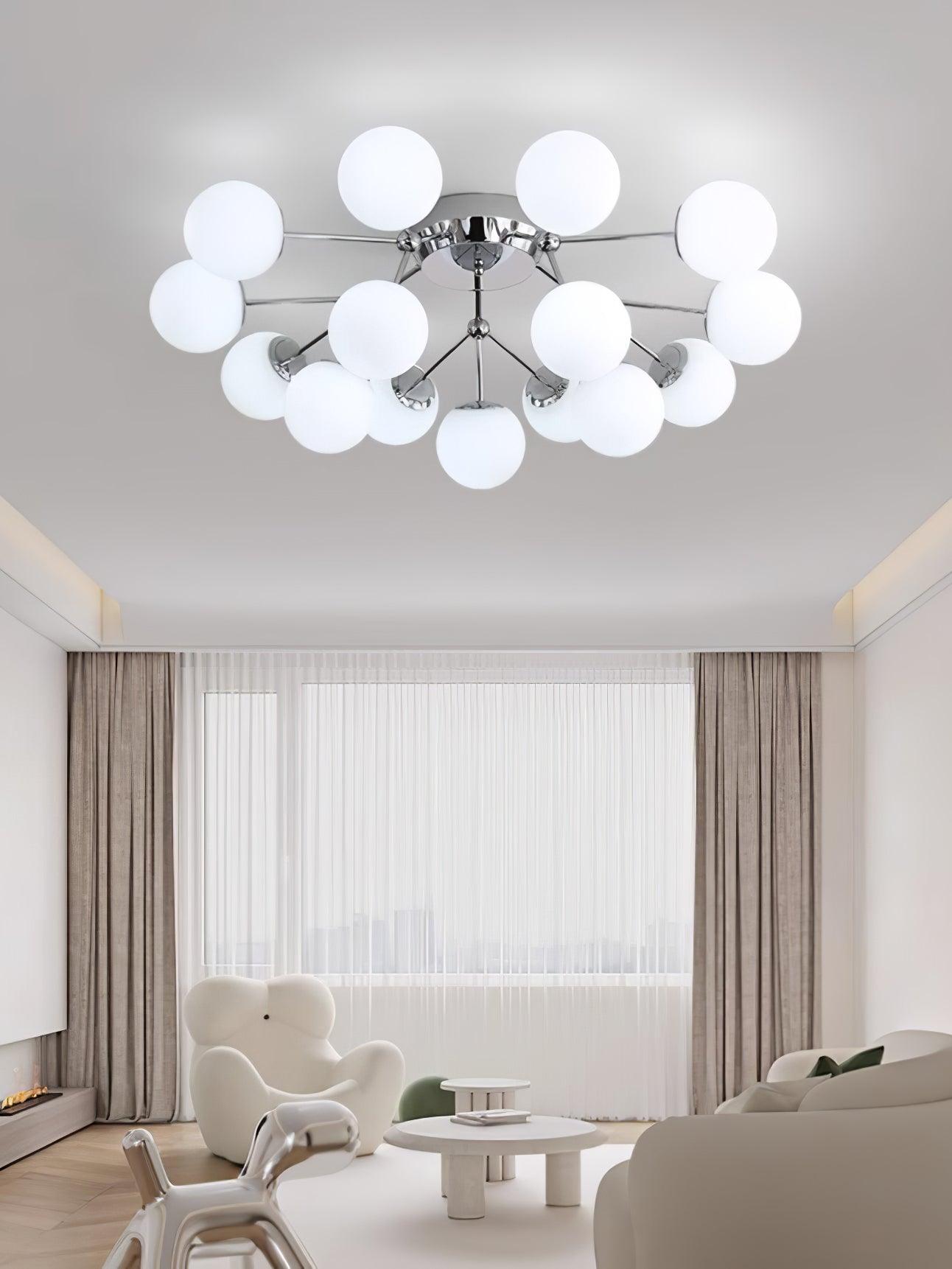White-lit chrome globe cluster above a living room with white lounge chair, curved sofa, layered tables and chrome sculpture