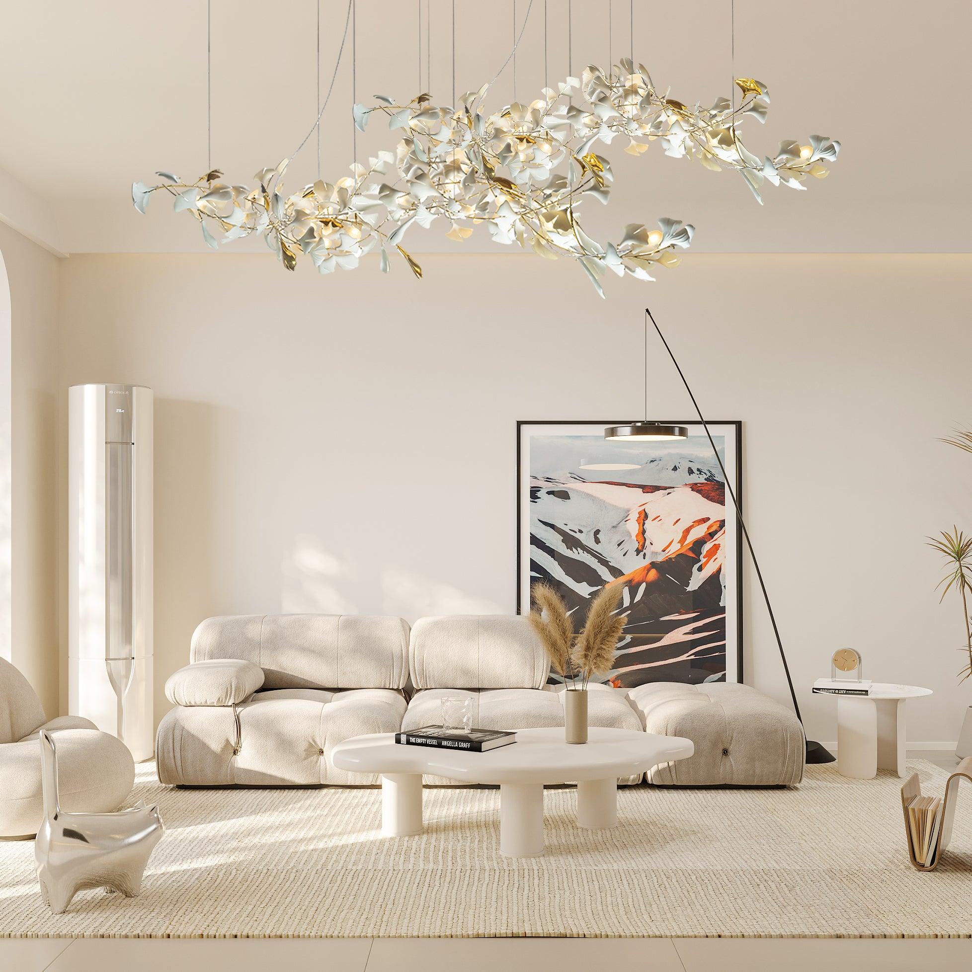 Gold-and-white leaf chandelier above a tufted cream sofa, irregular white table and mountain artwork