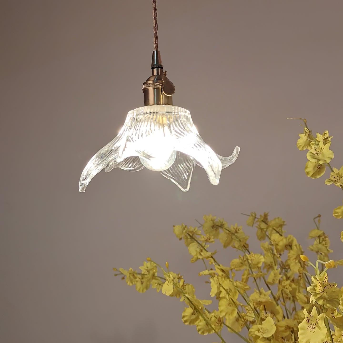 Low angled view of curling glass petals and a bright clear round bulb beside yellow flowers on grey.