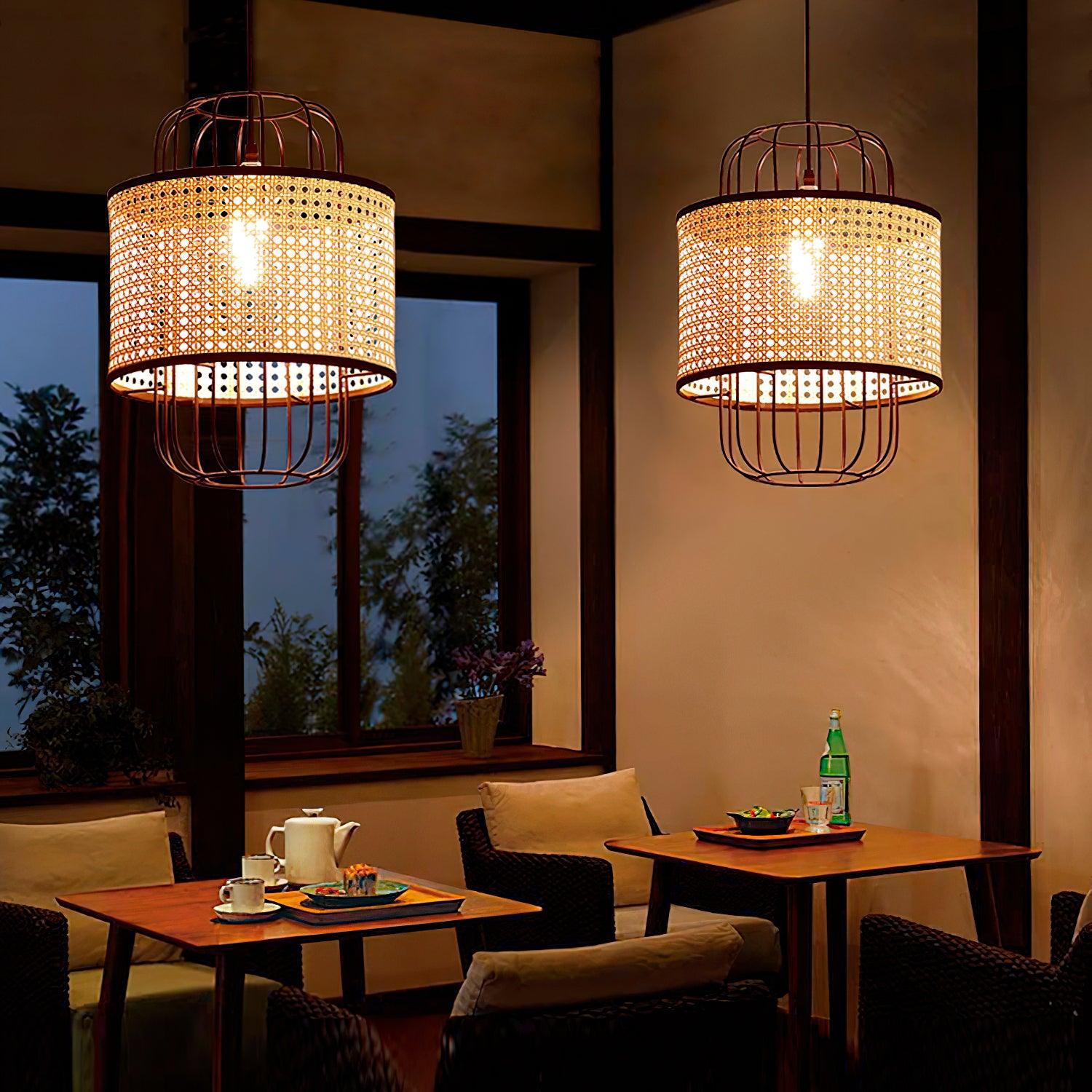 Two separate lit rattan cage pendants above booth tables beside windows at night