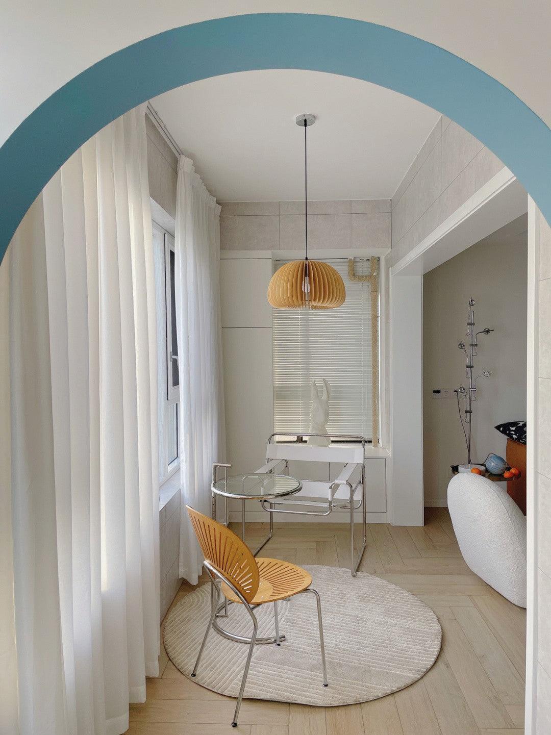 Unlit-looking wood slat pendant with a round ceiling canopy in a pale seating area viewed through a blue arch