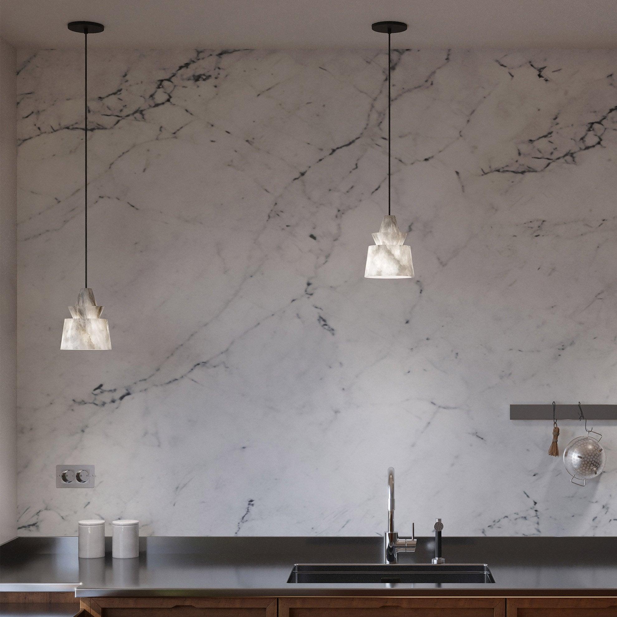 Two layered stone pendants at unequal drops above metal sink counter, pale veined wall, white canisters and hanging strainer.