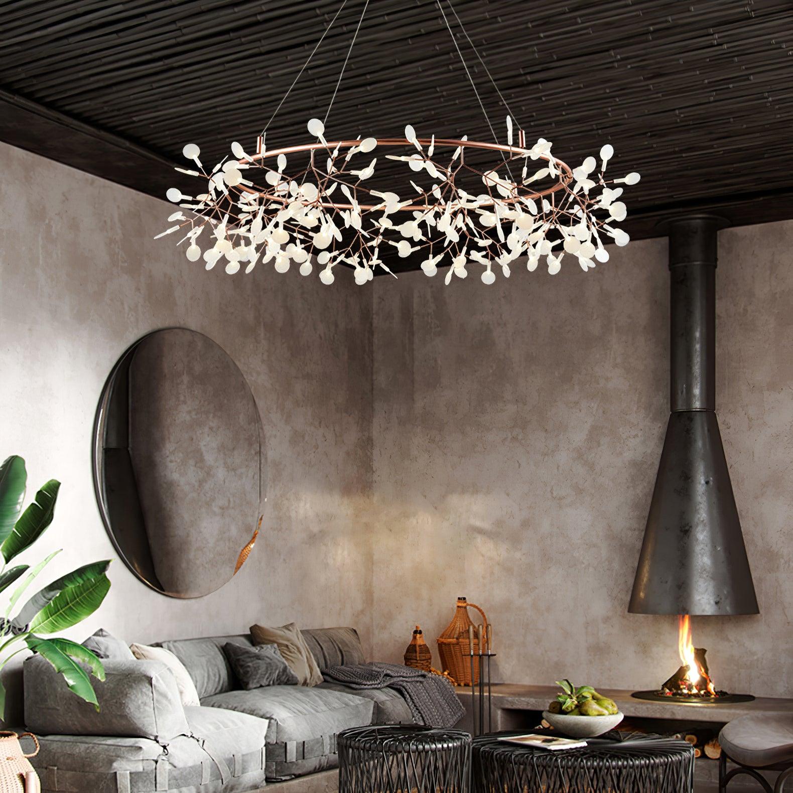 Rose-copper leaf ring chandelier above a distressed grey sofa near a round mirror and suspended fireplace
