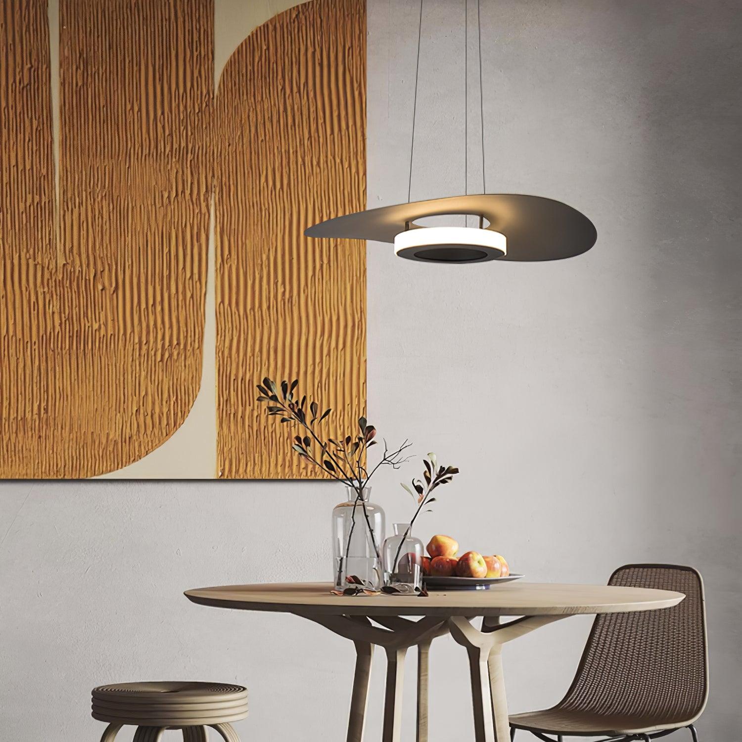 Dark curved disc light above round tree-leg table with apples and vases beneath gold-toned wall art