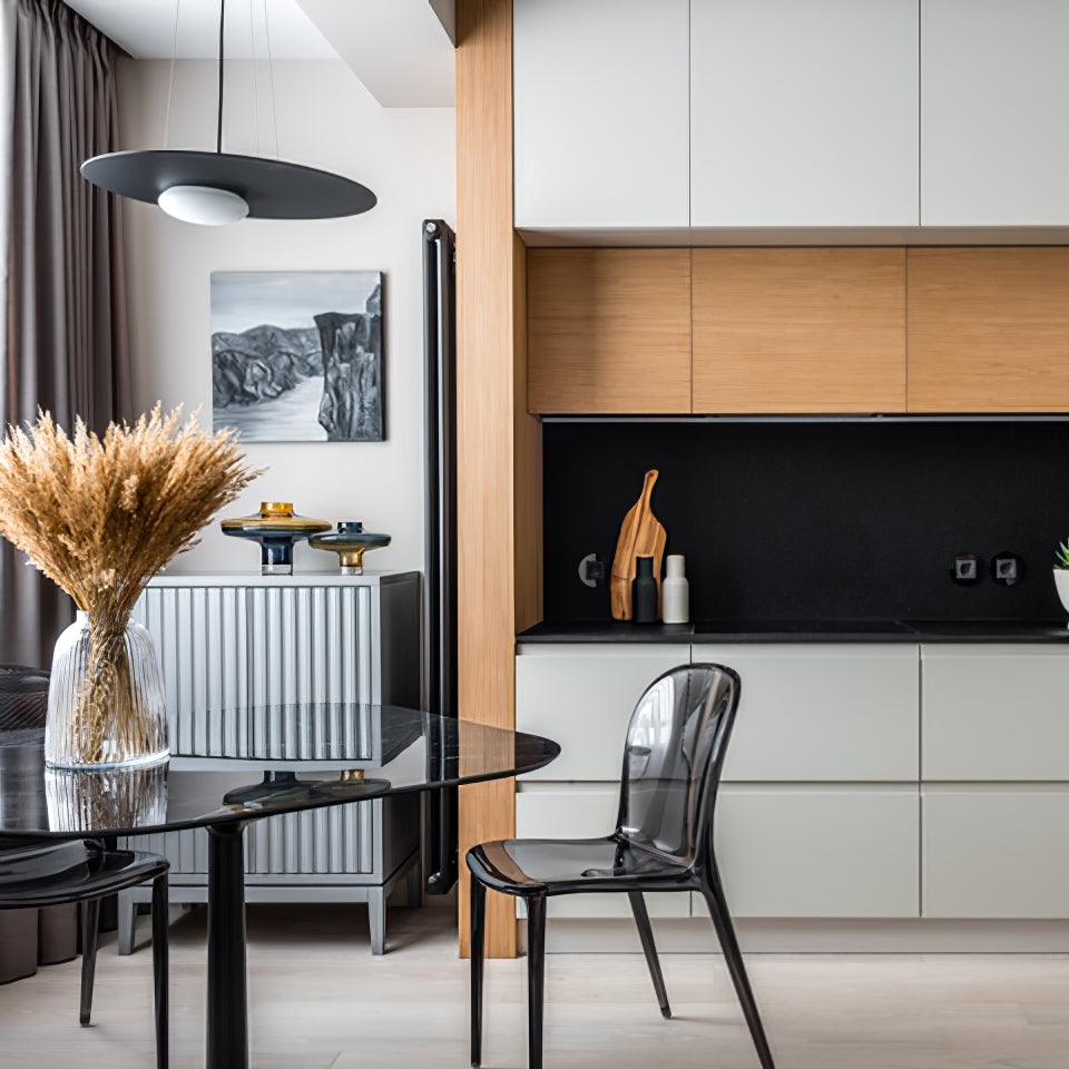 Black disc pendant over a glossy black dining table and dried-grass vase, beside dark transparent chair and wood-and-white cabinetry.