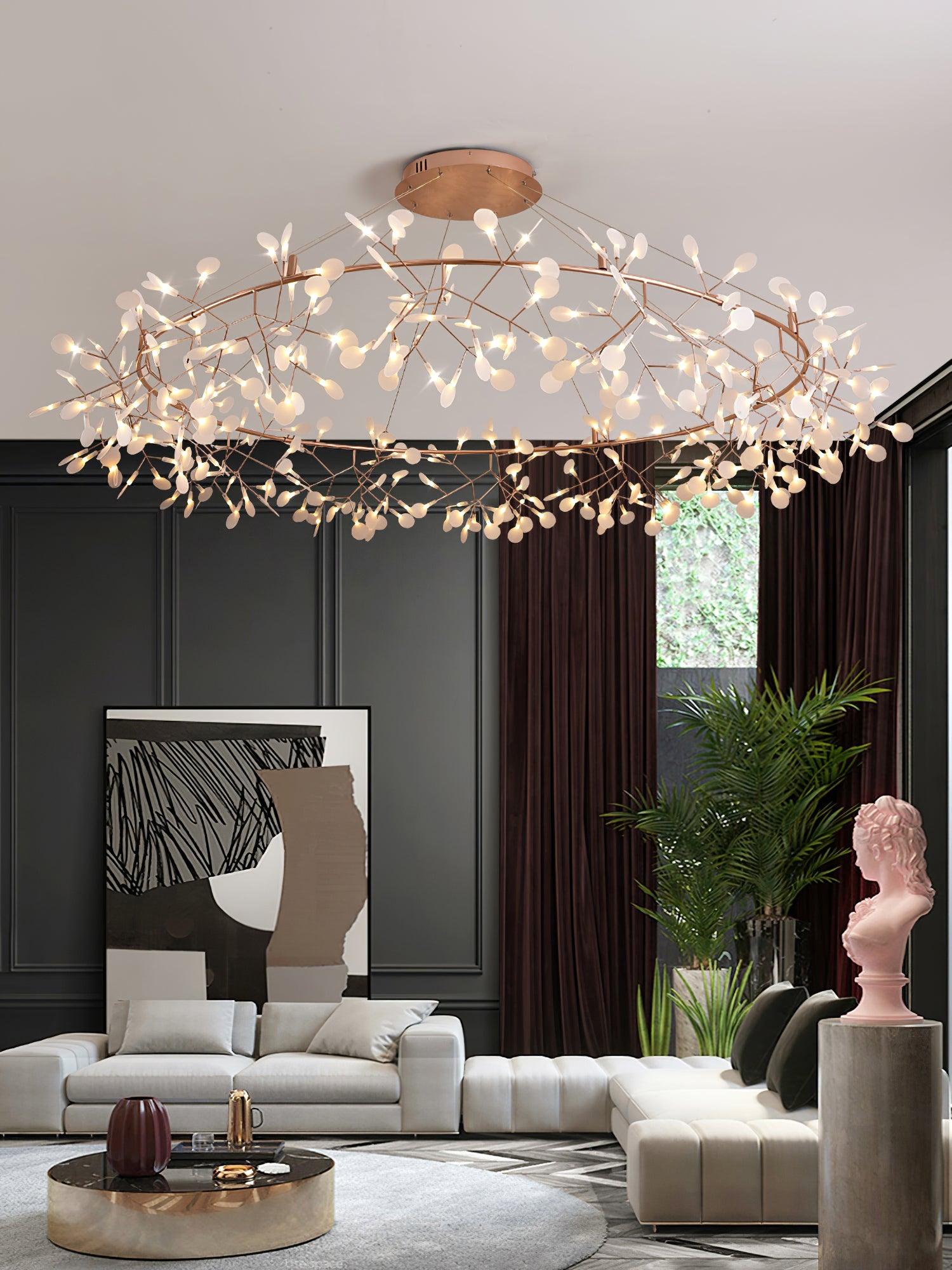 Wide warm metallic leaf ring chandelier above grey seating, abstract artwork, a palm and a pink bust