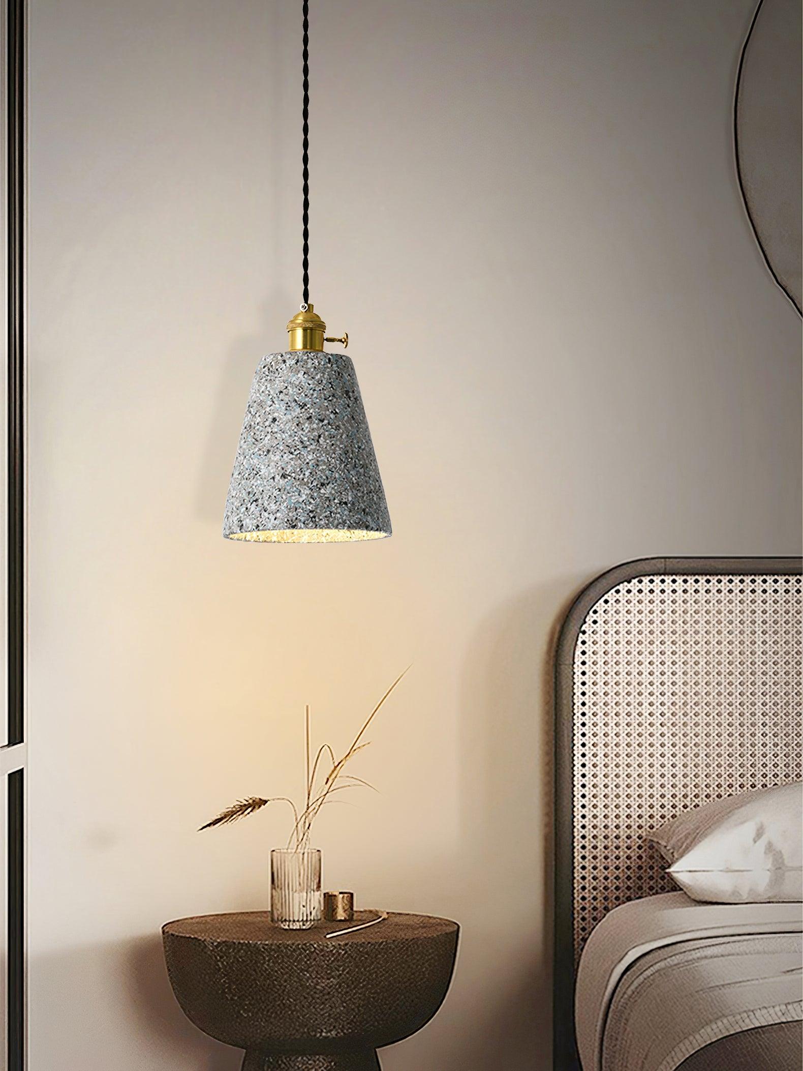 Tall tapered cement pendant above a bedside table