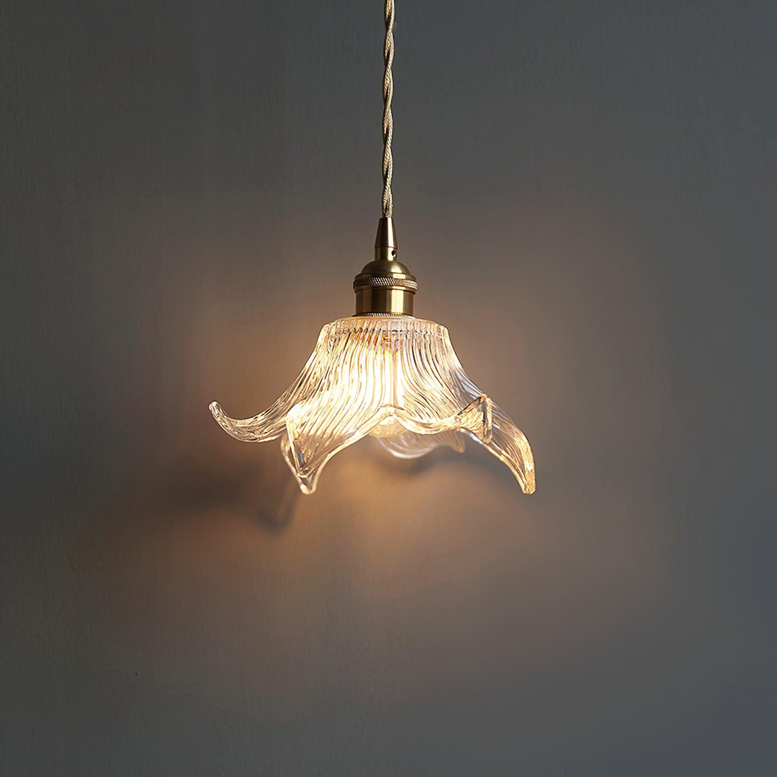 Single illuminated petal shade and brass-toned holder against a rough dark grey wall, with warm glow behind.