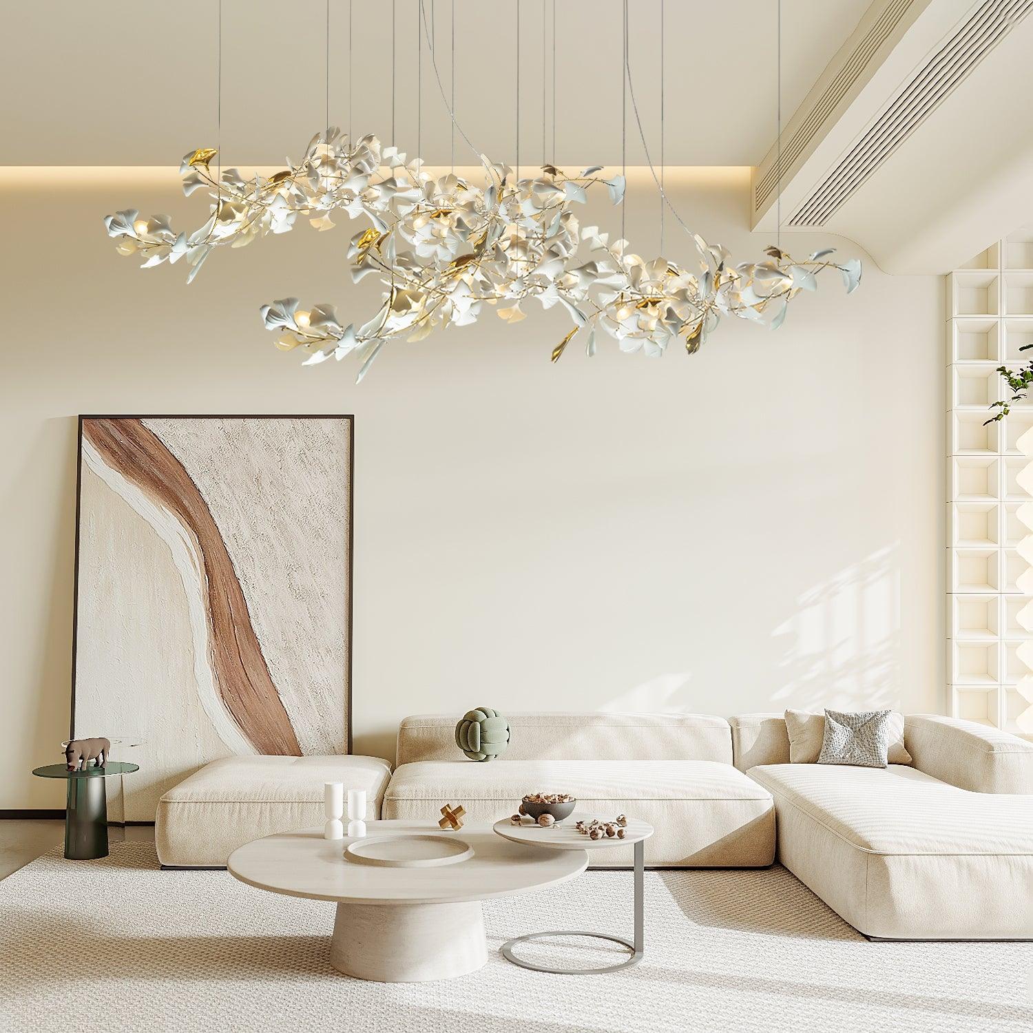 Gold-and-white ginkgo chandelier above a cream L-shaped sofa, round tables and curved brown artwork