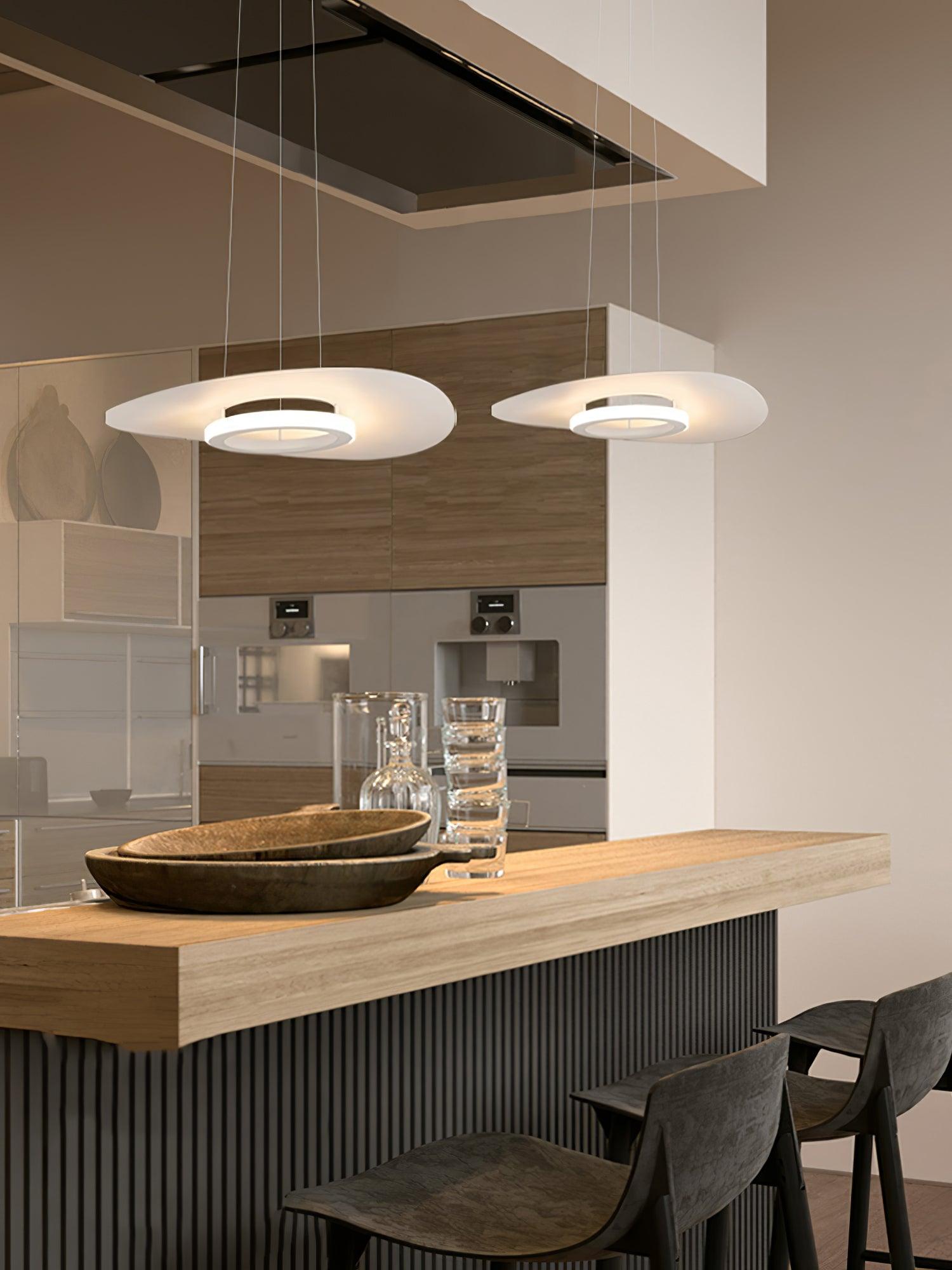 Two White disc pendants above wood-topped kitchen counter with bowls, glass carafes and ovens behind