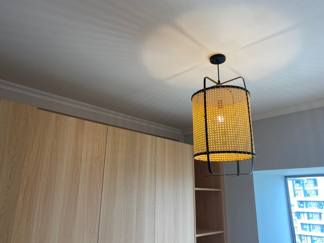 Single glowing cane pendant with short black suspension above wood wardrobes, casting patterns on the ceiling