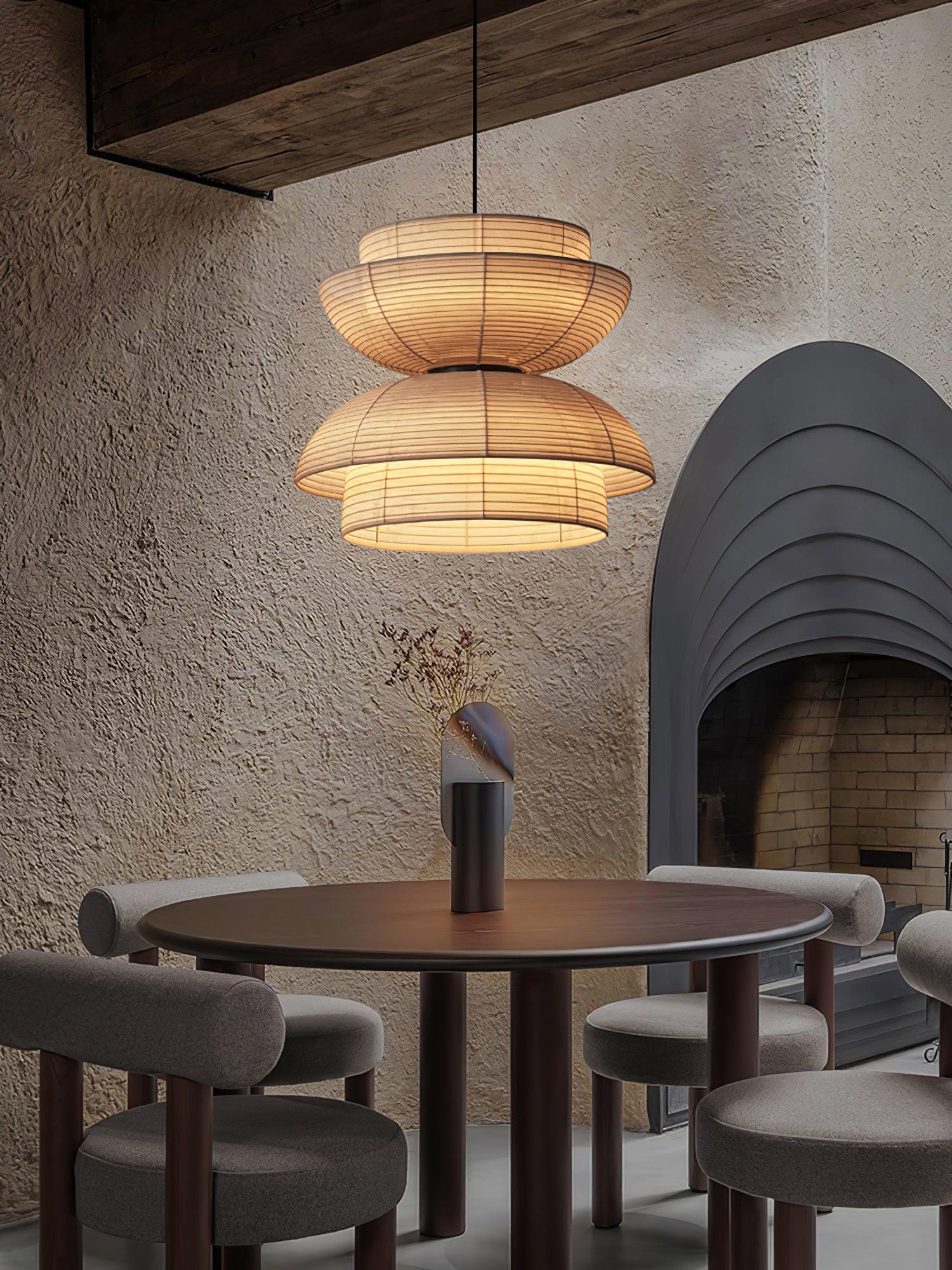 Portrait of a lit fabric pendant over a round table beside a grey arched fireplace and textured wall