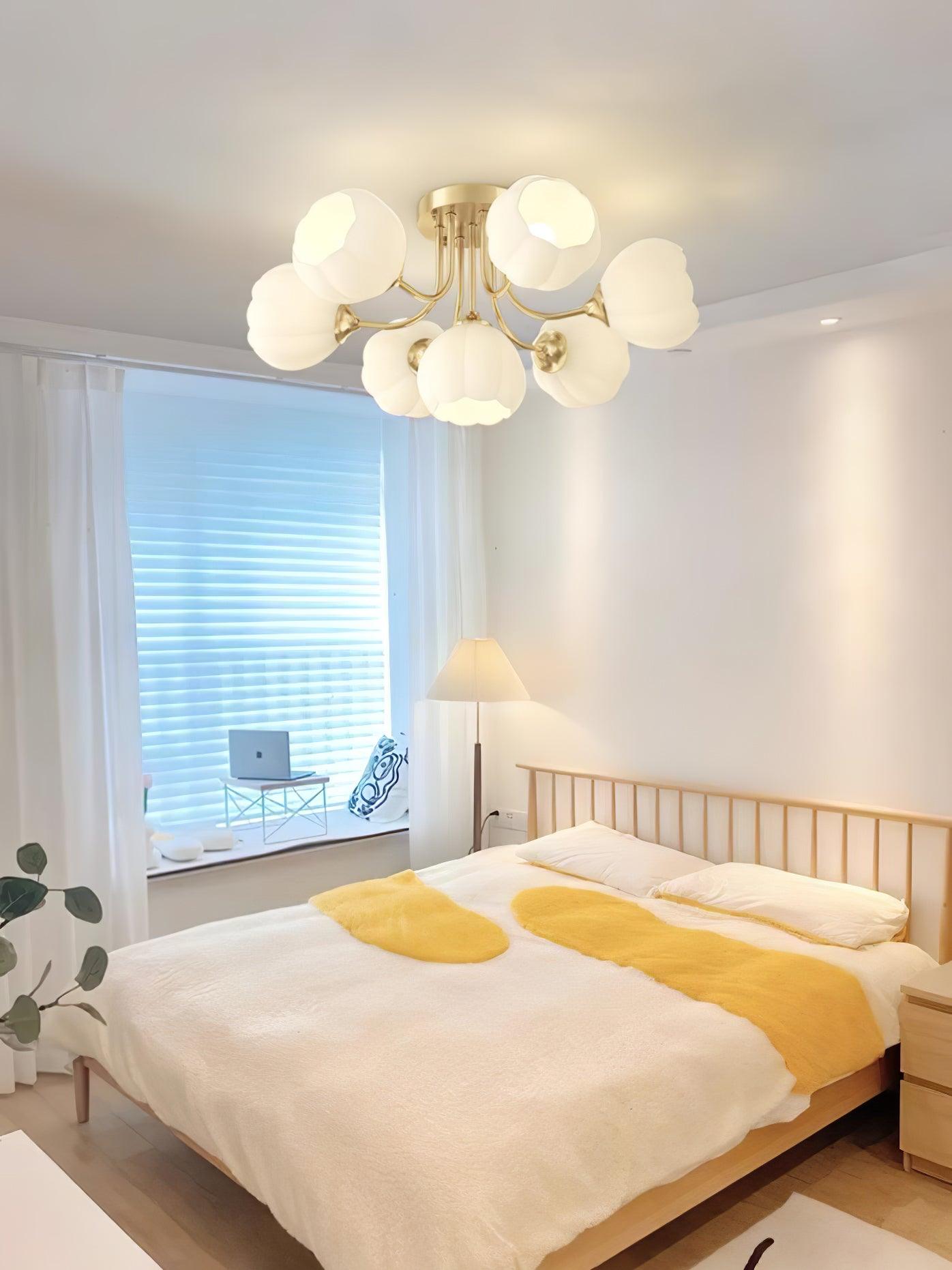 Pumpkin ceiling light with brass-colour arms and white glass shades above a bed with yellow and white linen