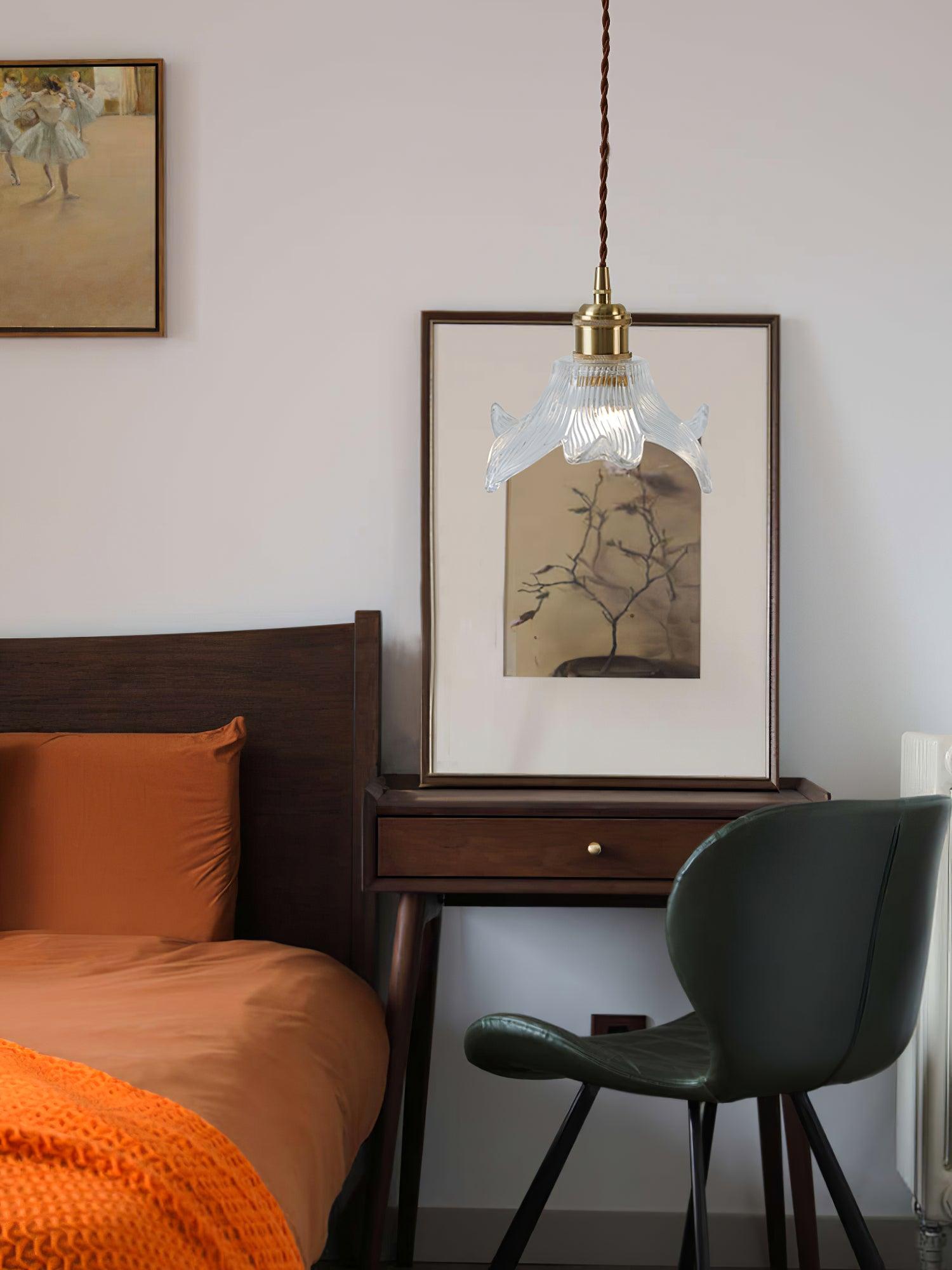 Lit glass petal pendant beside a dark wooden bed with orange bedding, framed tree artwork and a green chair.