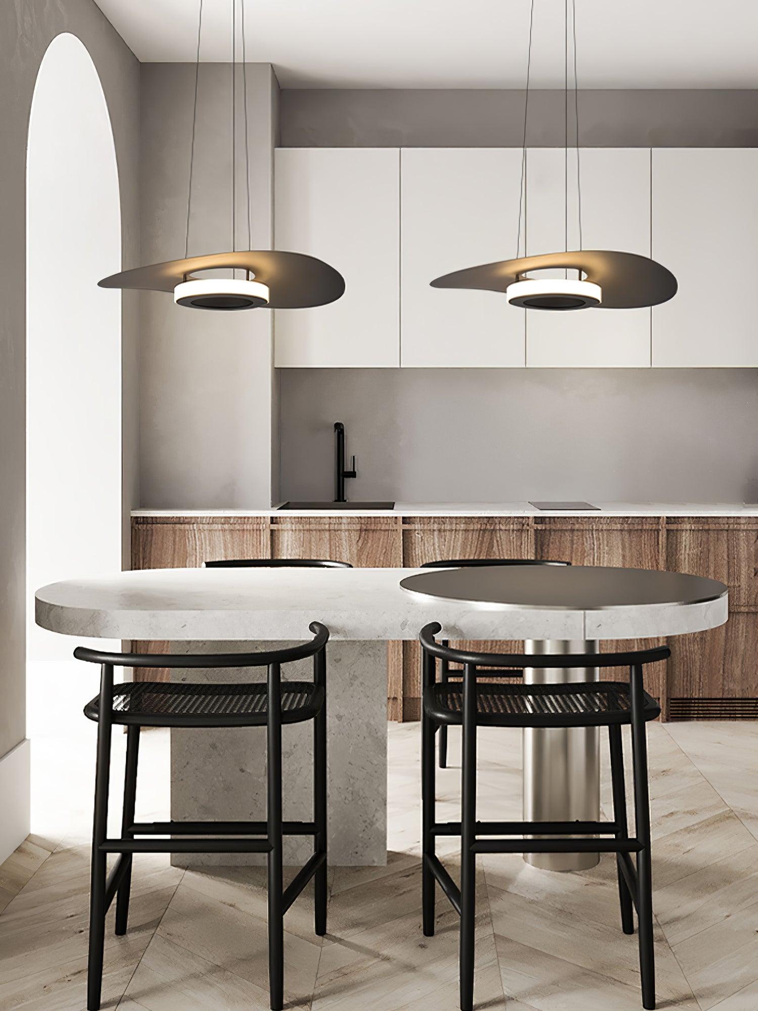 Paired dark disc lights above rounded stone island table, black stools and white-and-wood kitchen cabinets