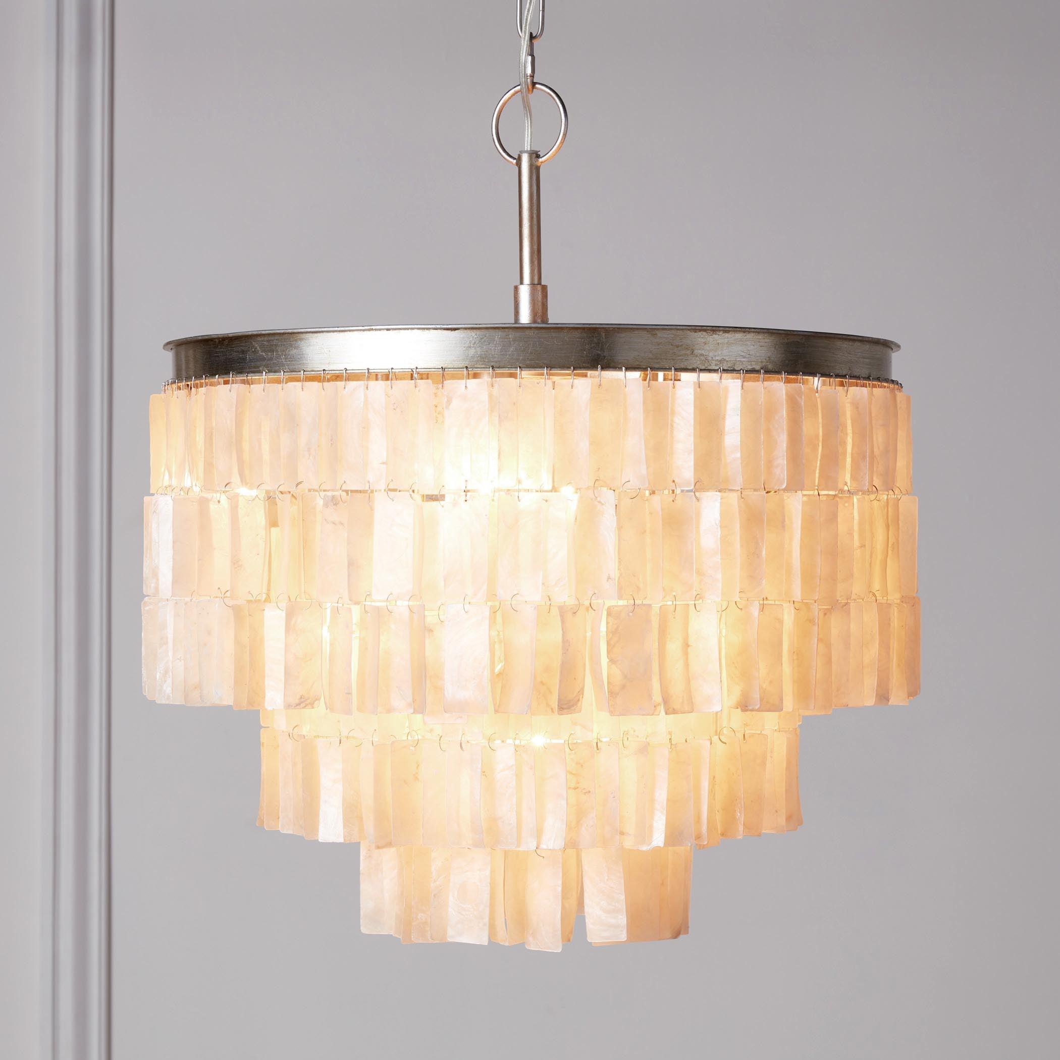 Lit close-up of rectangular shell tiers beneath a silver top band, short stem and chain against a pale wall