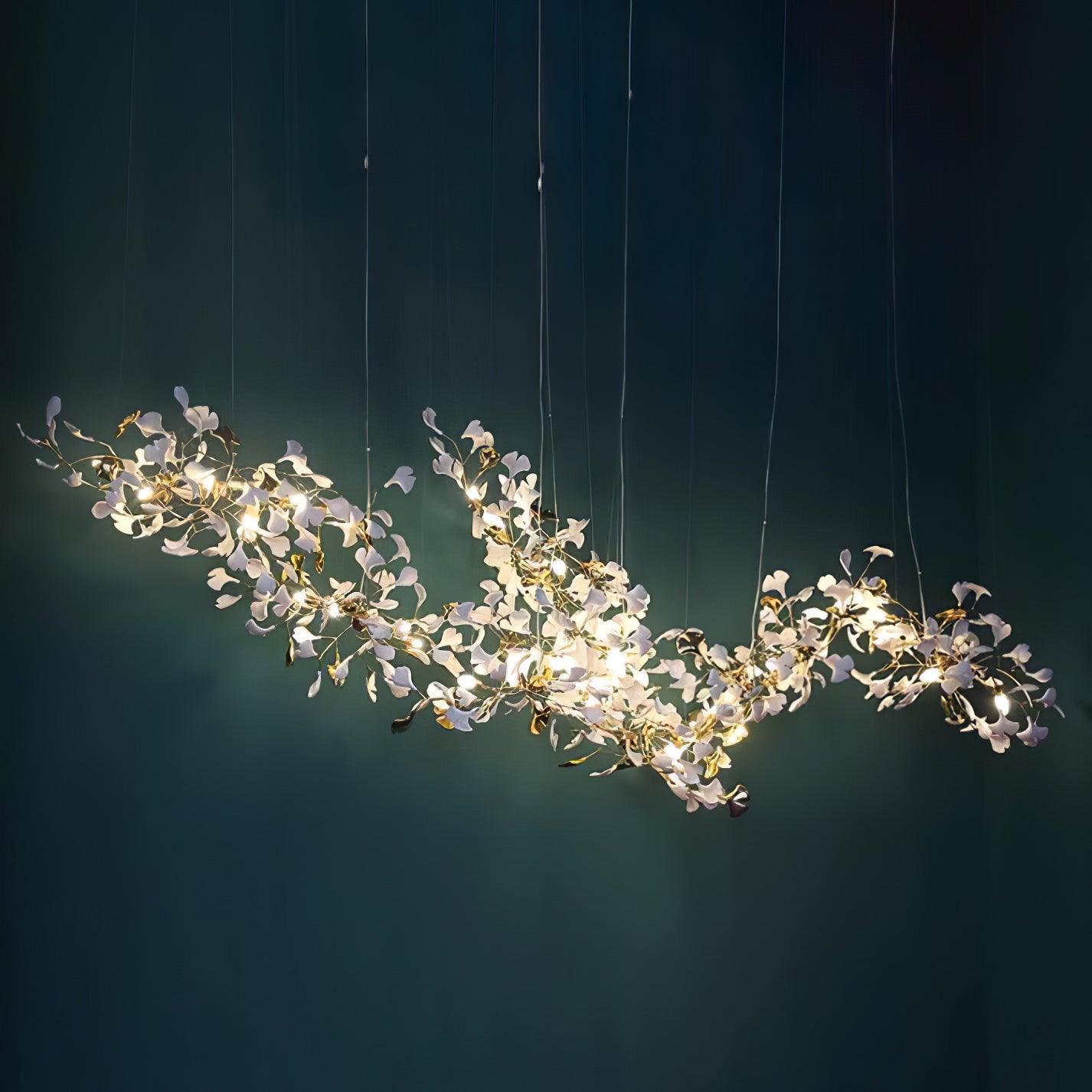 Long gold-and-white ginkgo chandelier lit against a deep teal wall with fine suspension wires