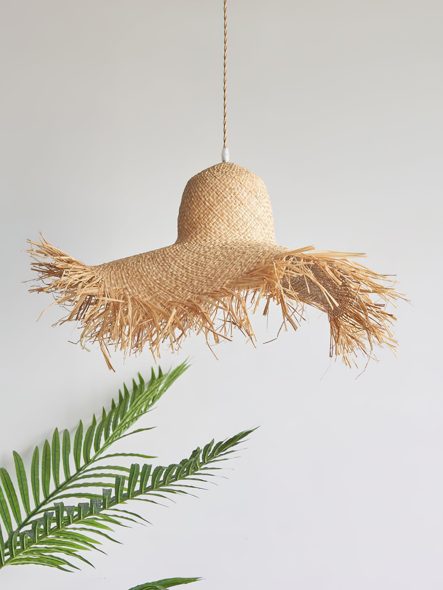 Unlit woven hat shade with rounded crown, uneven fringed brim and tan cord above palm fronds