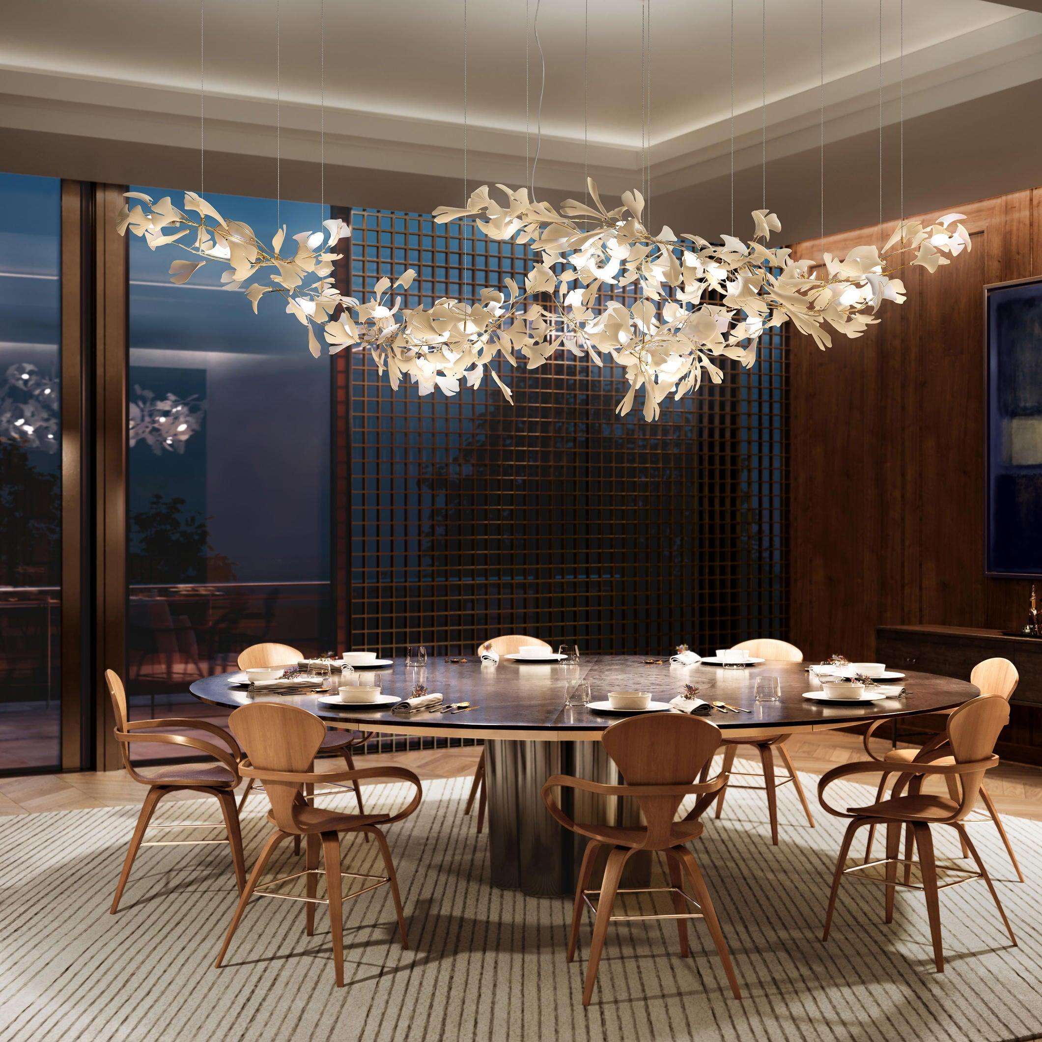 White ginkgo leaf chandelier above a dark oval timber dining table against a lattice wall and tall blue window