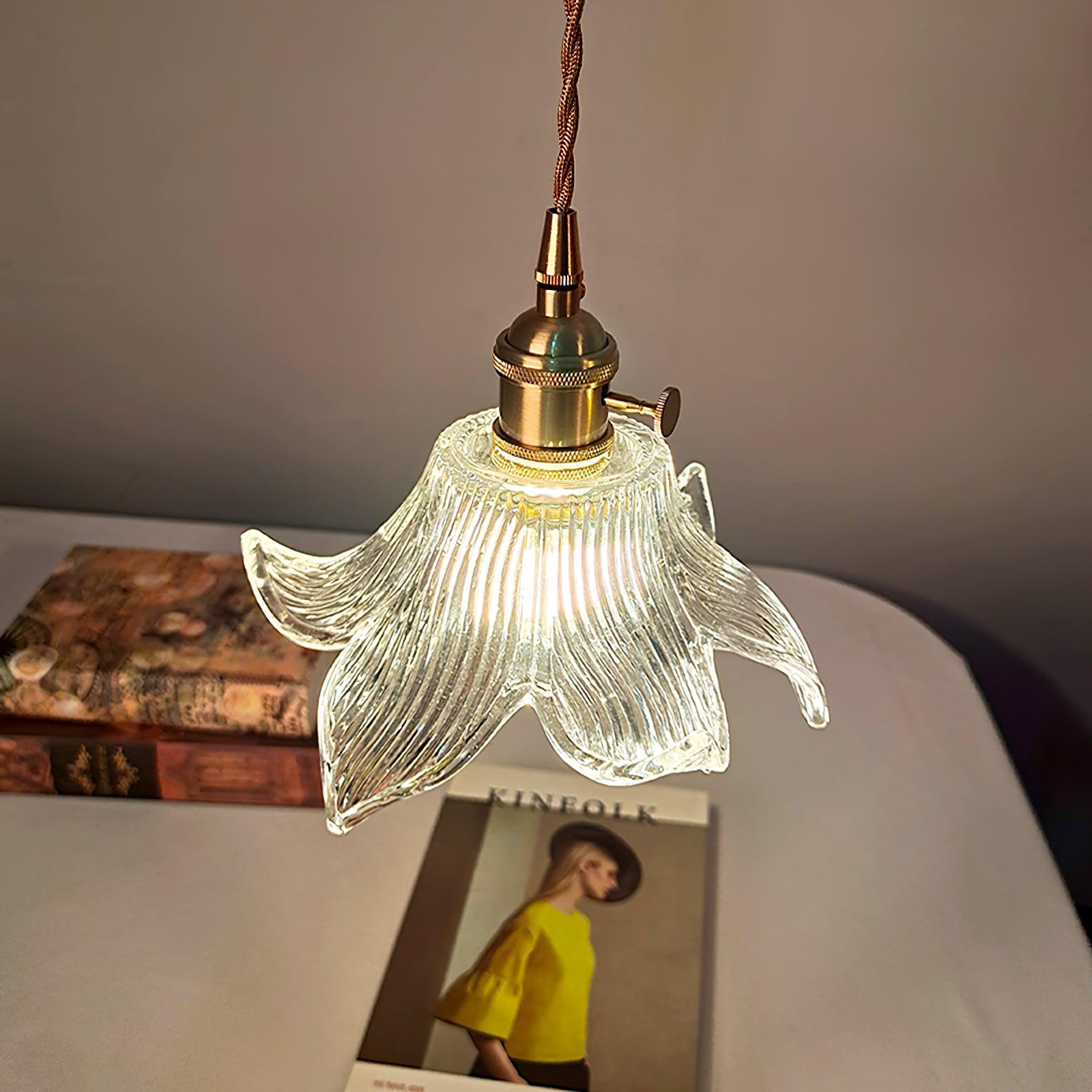 Angled lit petal glass shade above a white round table with patterned books and a yellow-cover Kinfolk magazine; small side knob visible.