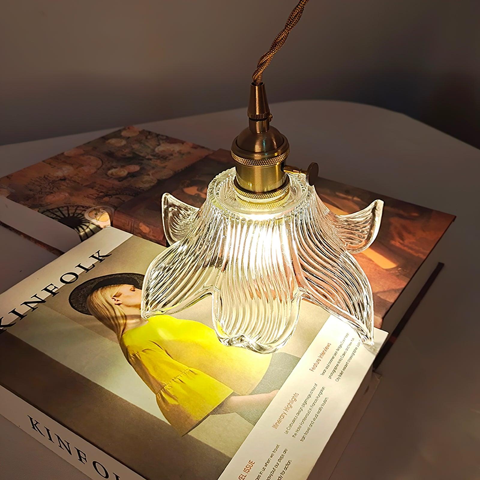 High angled view of the illuminated glass petals and small side knob above books and a yellow-cover Kinfolk magazine.