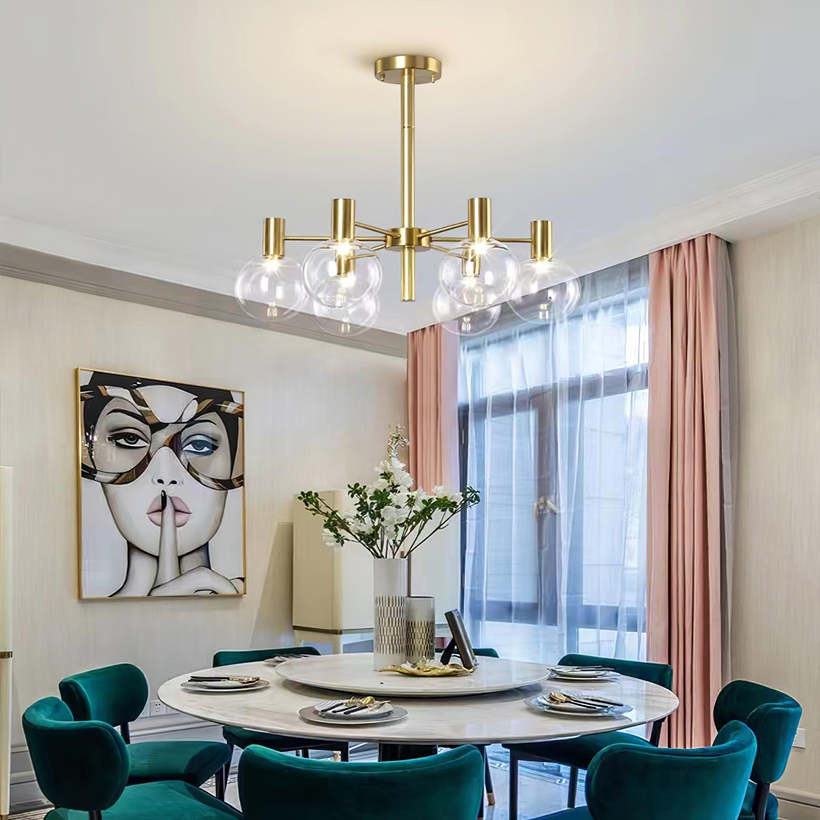 Clear-globe chandelier above a round dining table with teal chairs, pink curtains, white flowers and framed face artwork.