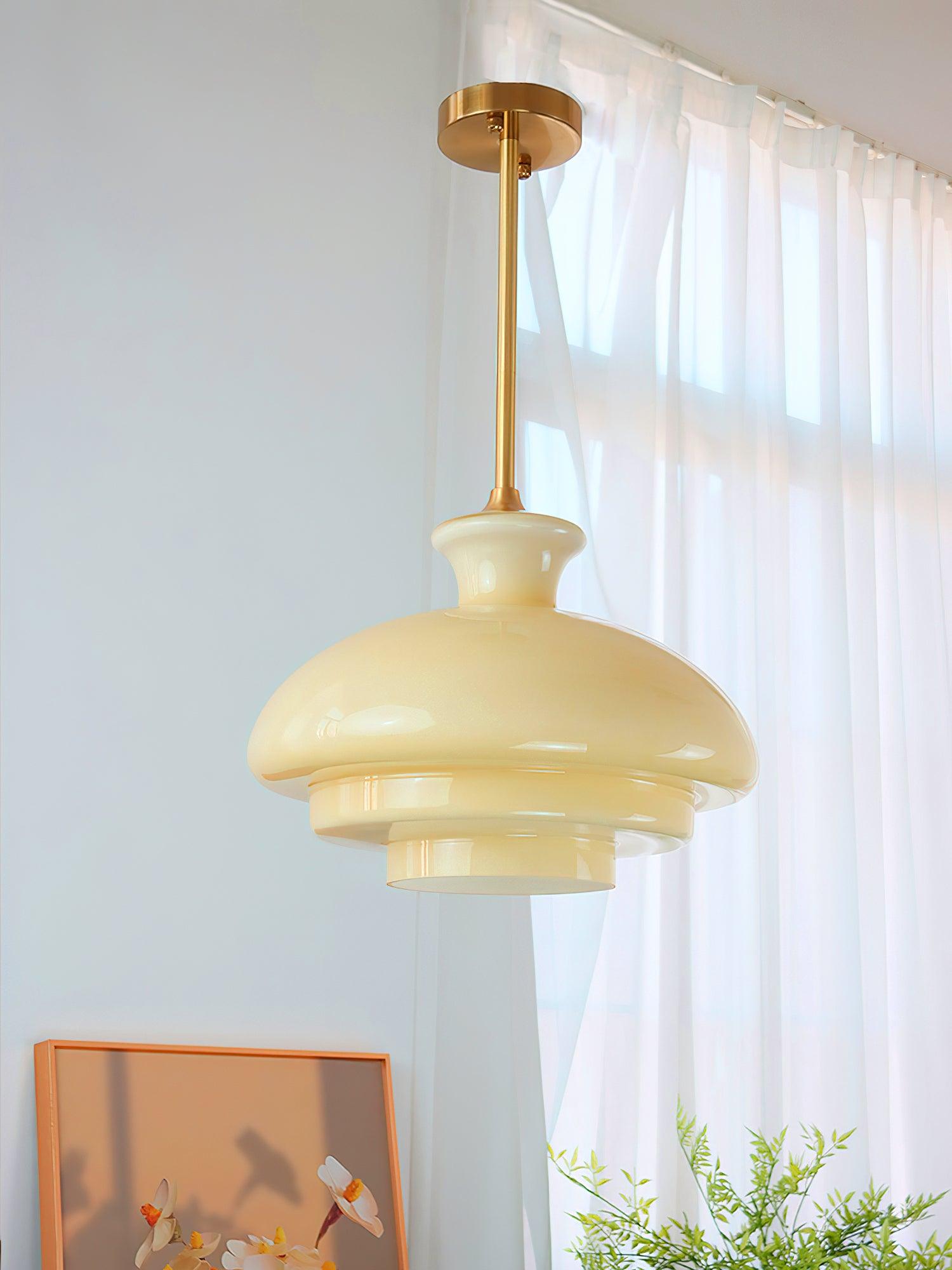 Yellow glass pendant near a window and white curtains with orange framed artwork and flower props