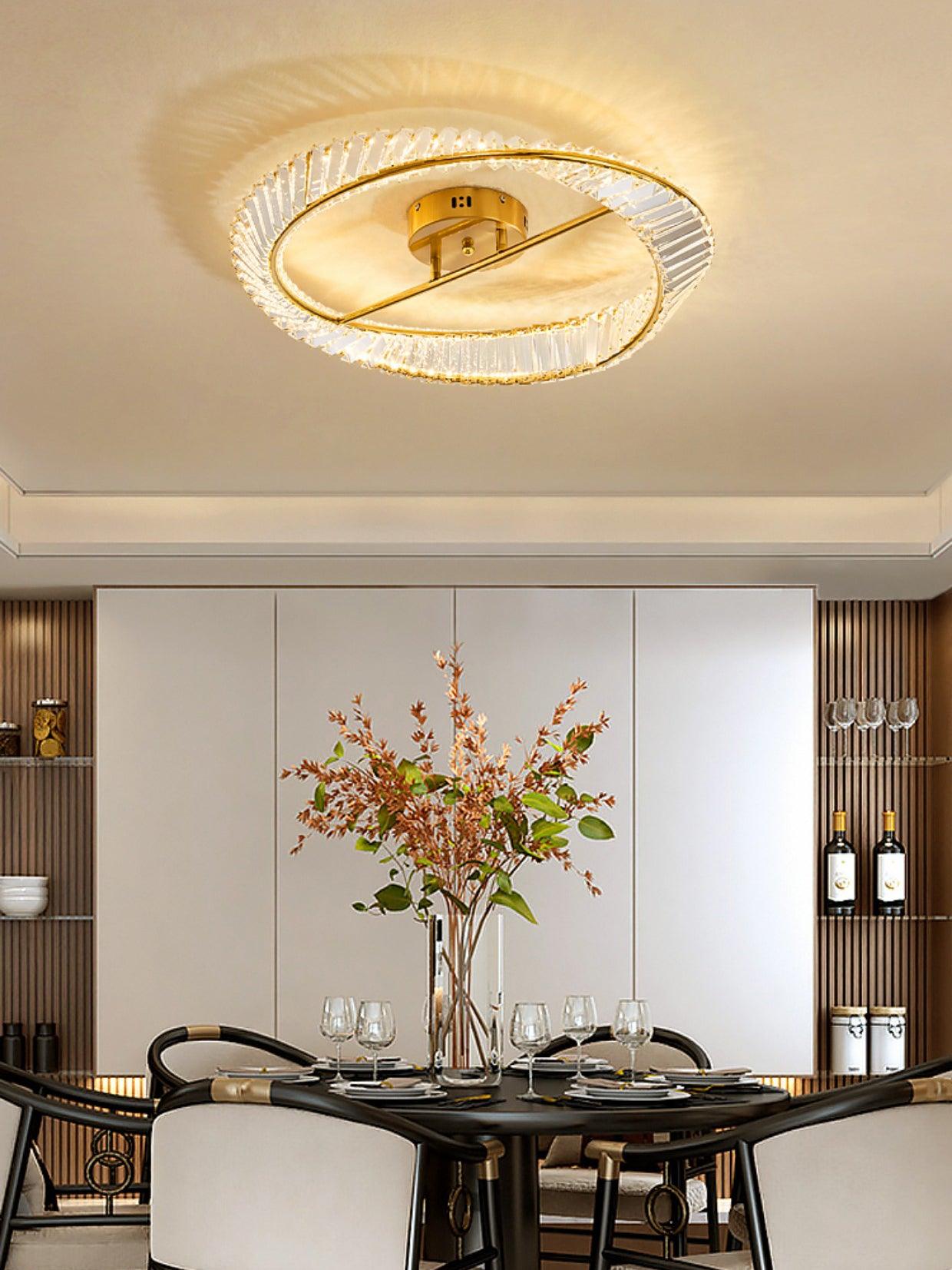 Gold-tone glass ring light above a black dining table with white chairs and a tall floral vase