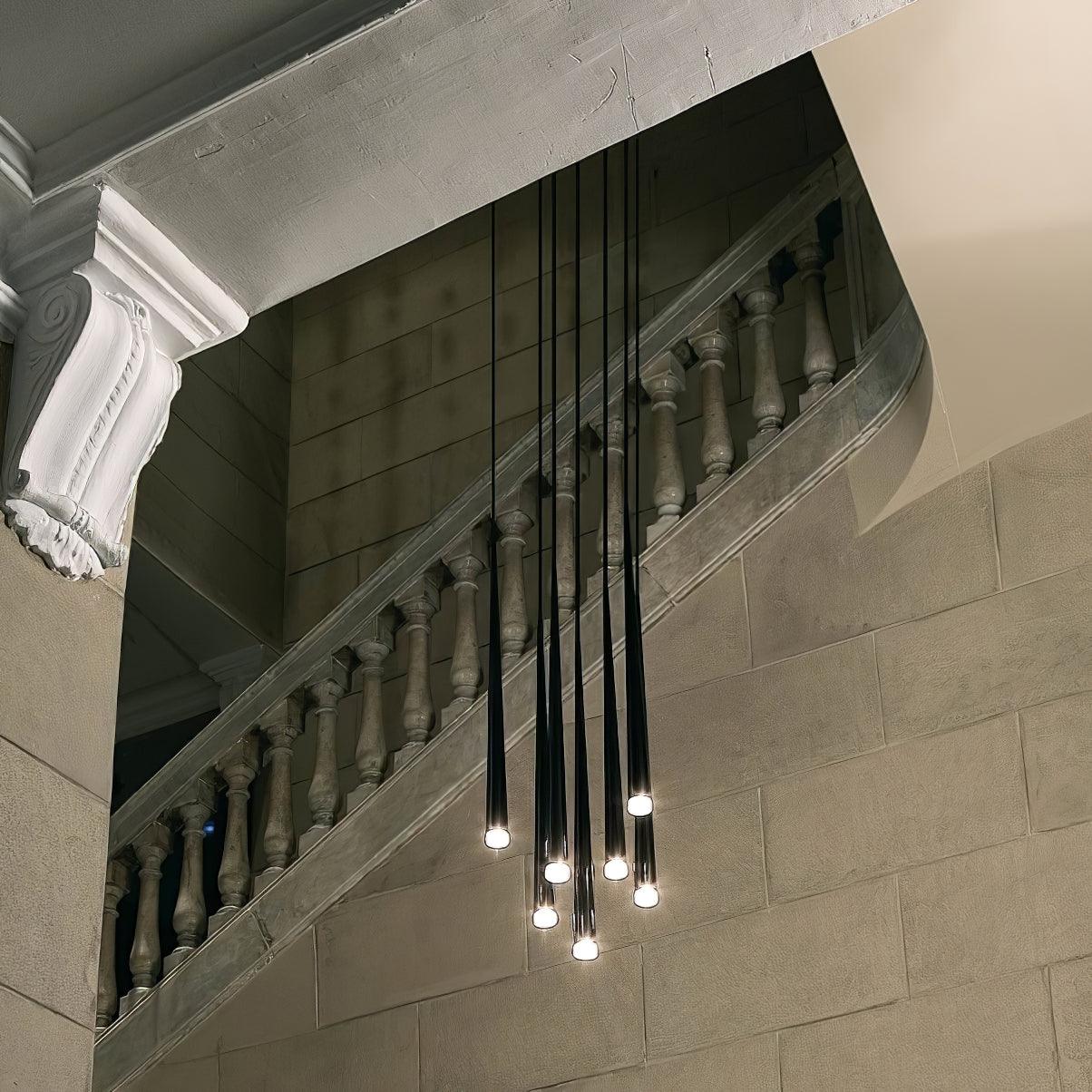 Six glowing black tube pendants clustered beside a stone staircase and carved balustrade