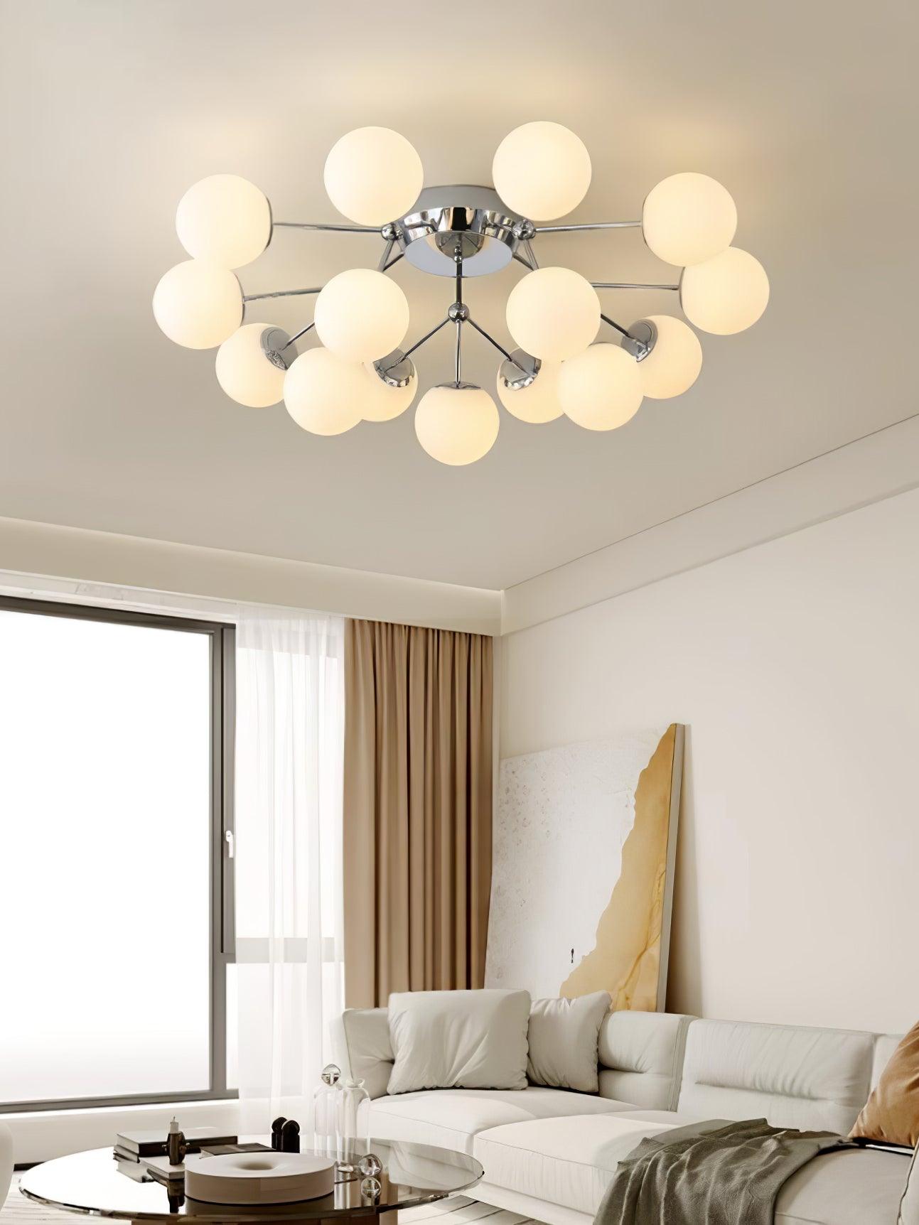 Warm-lit chrome globe cluster above a white sofa, round glass coffee table and tall cream artwork beside a curtained window