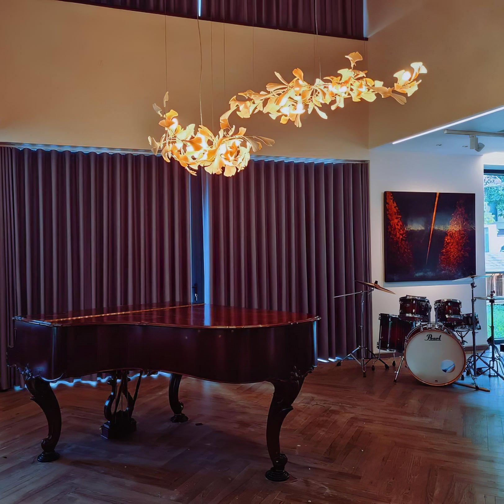 Two separate white branching leaf chandeliers at different heights above a grand piano and drum kit beside tall windows
