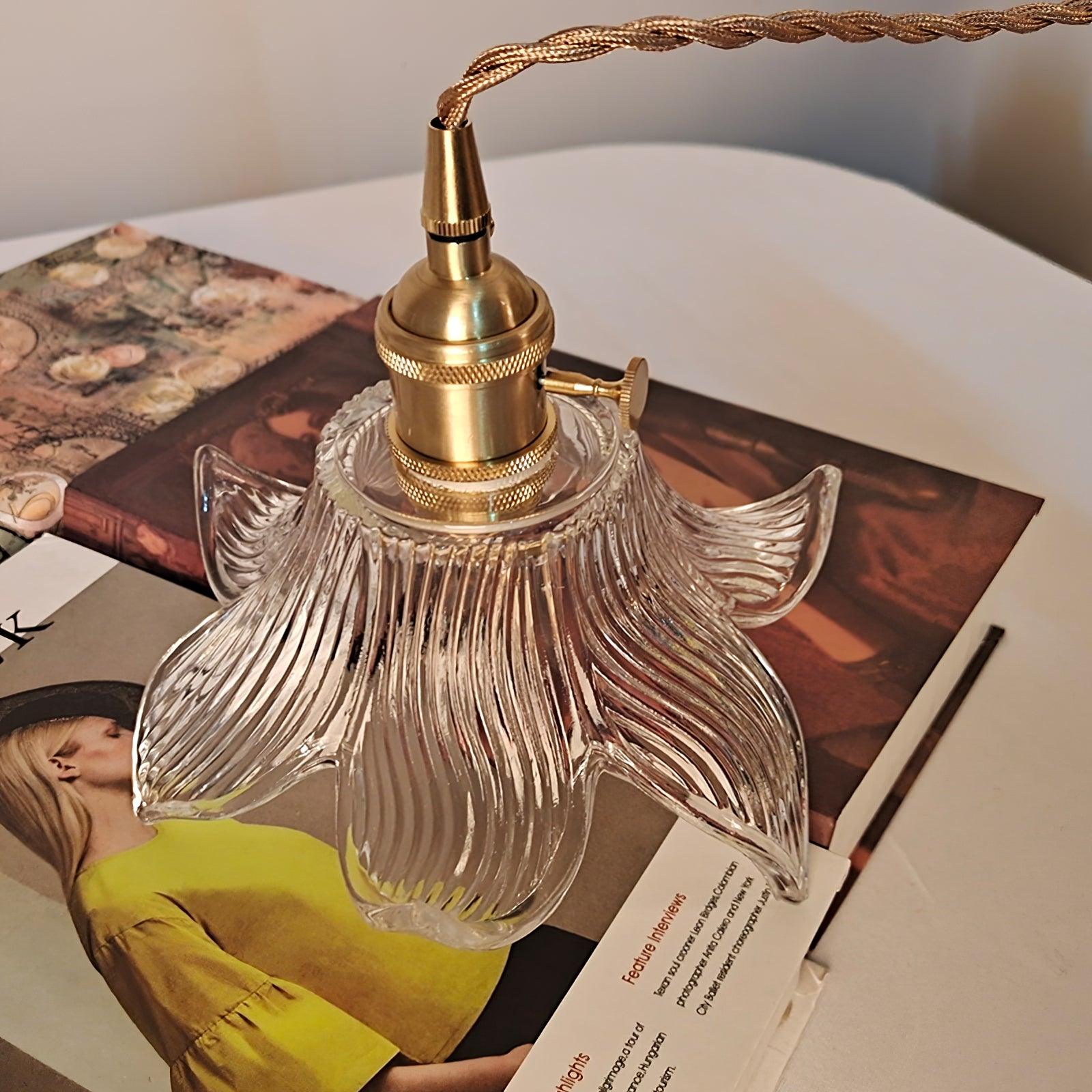 Brass-toned cylindrical holder with domed cap, knurled rings and round side knob above clear petals, resting on illustrated books.