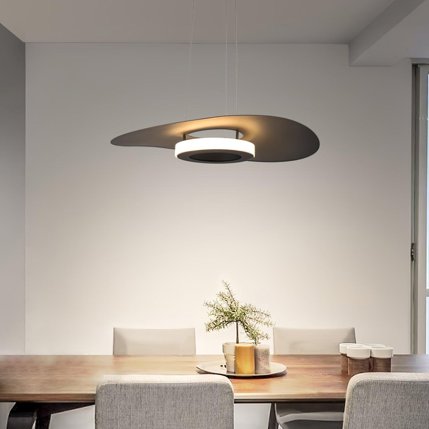Dark sculpted disc light over wooden dining table with grey chairs, tray, branch vase and cups