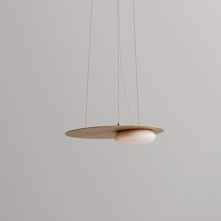 Unlit gold-tone disc and offset pale diffuser against grey, with fine suspension wires and pale power cord; canopy outside frame.
