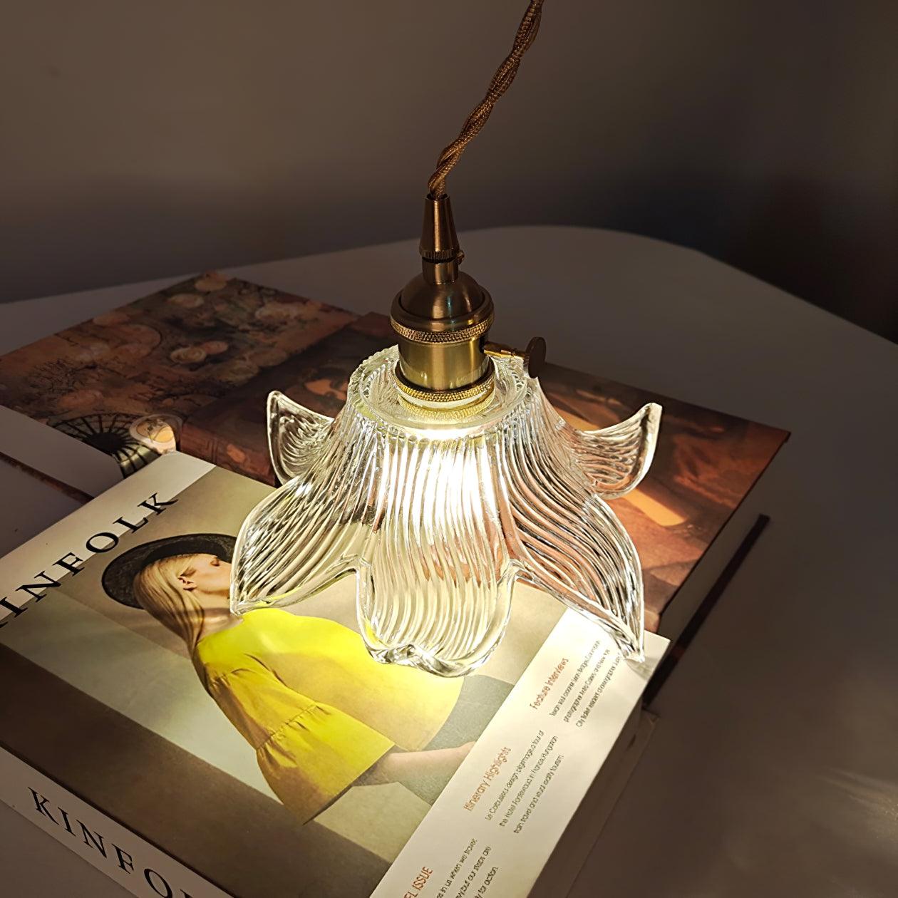 Illuminated flower glass shade and twisted cord above a yellow-dress magazine cover on a white round table.
