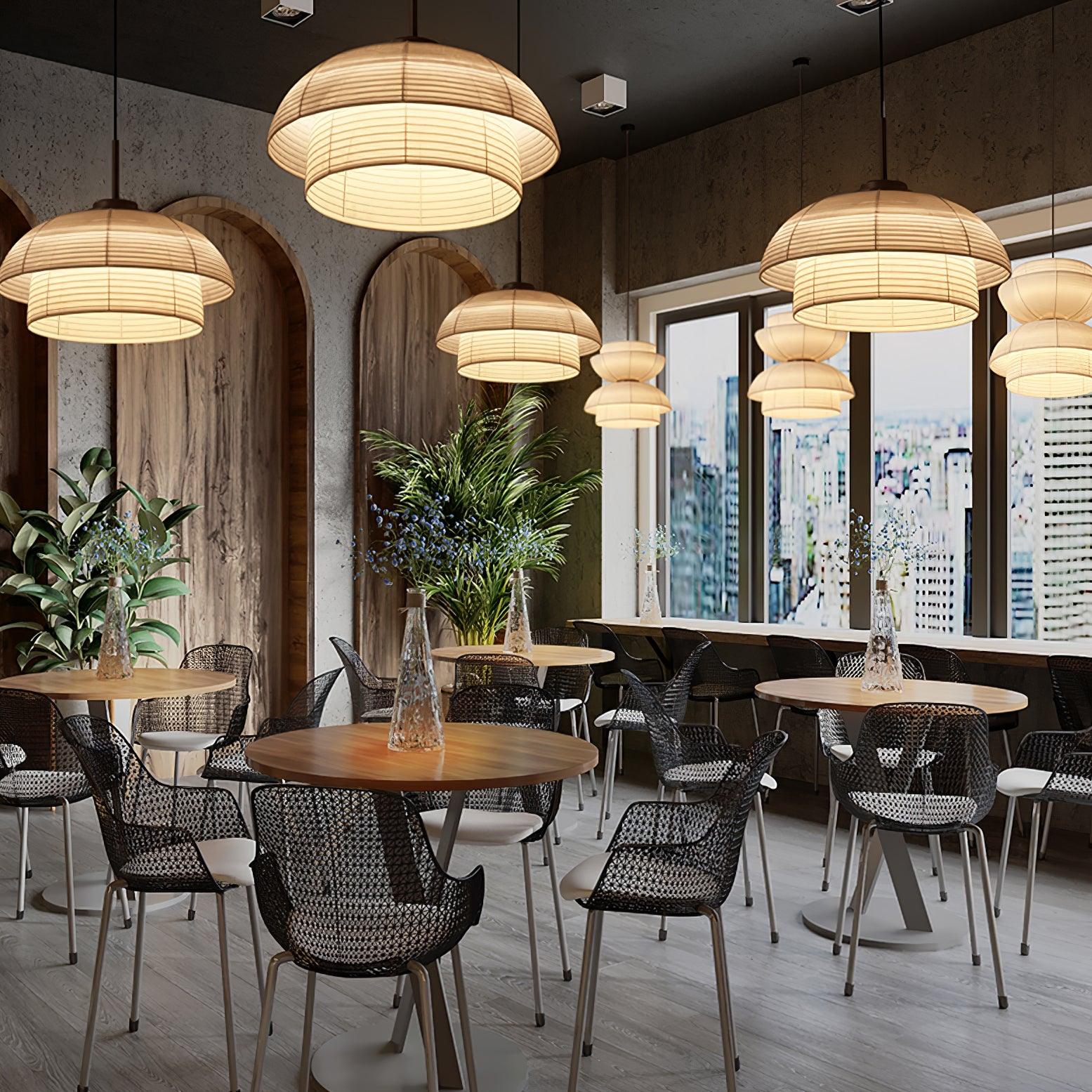 Multiple separate beige fabric pendants over cafe tables, with woven-look chairs, plants and large windows