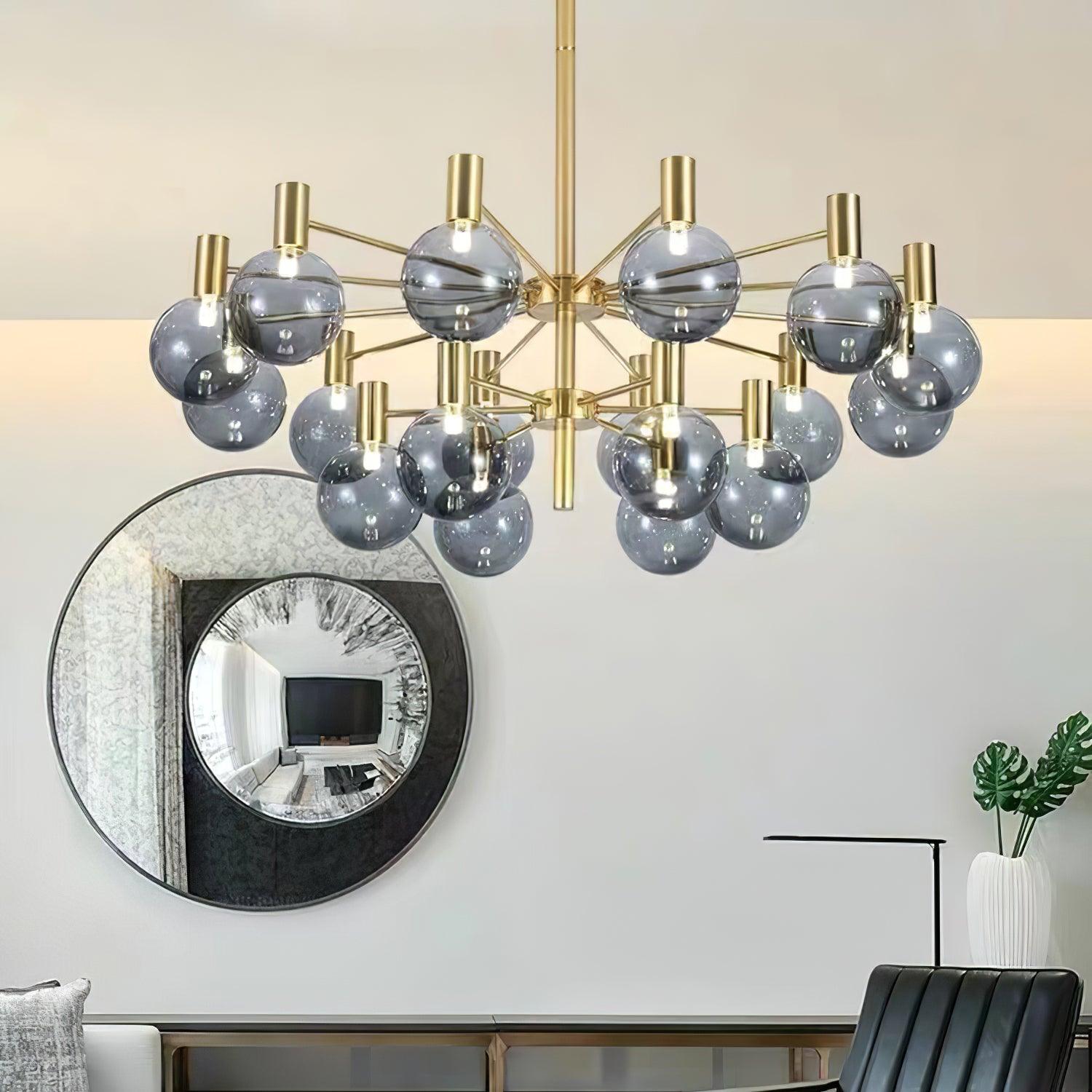 Two-tier clear-globe chandelier reflecting blue-grey tones, beside a large round mirror, pale sofa and black chair.
