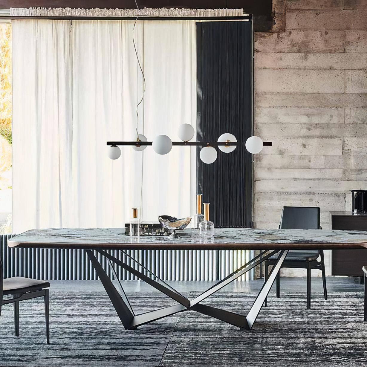 Globe pendant over green-grey veined table, clear bottles and bowl, beside sheer curtain, radiator and concrete wall.