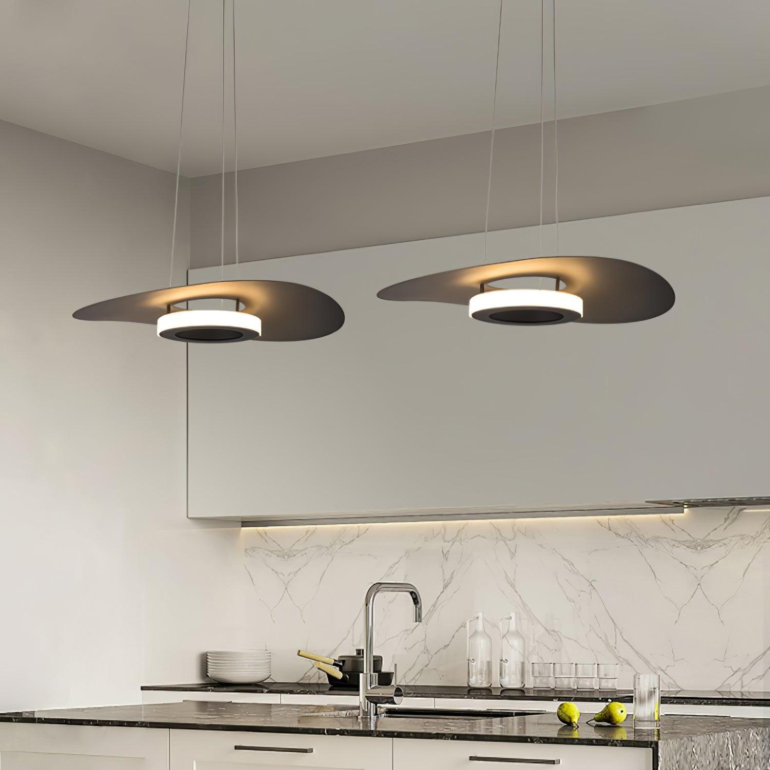 Two dark disc pendants over marble-veined sink counter with bottles, glassware and pears