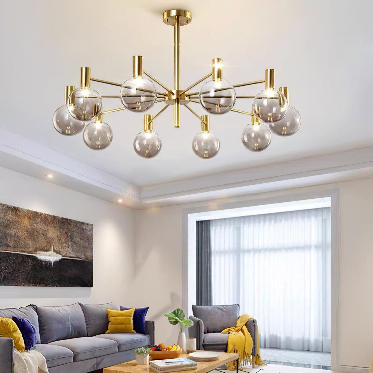 Clear-globe chandelier above a grey sofa and armchair with yellow accents, beside abstract art and a sheer-curtained window.