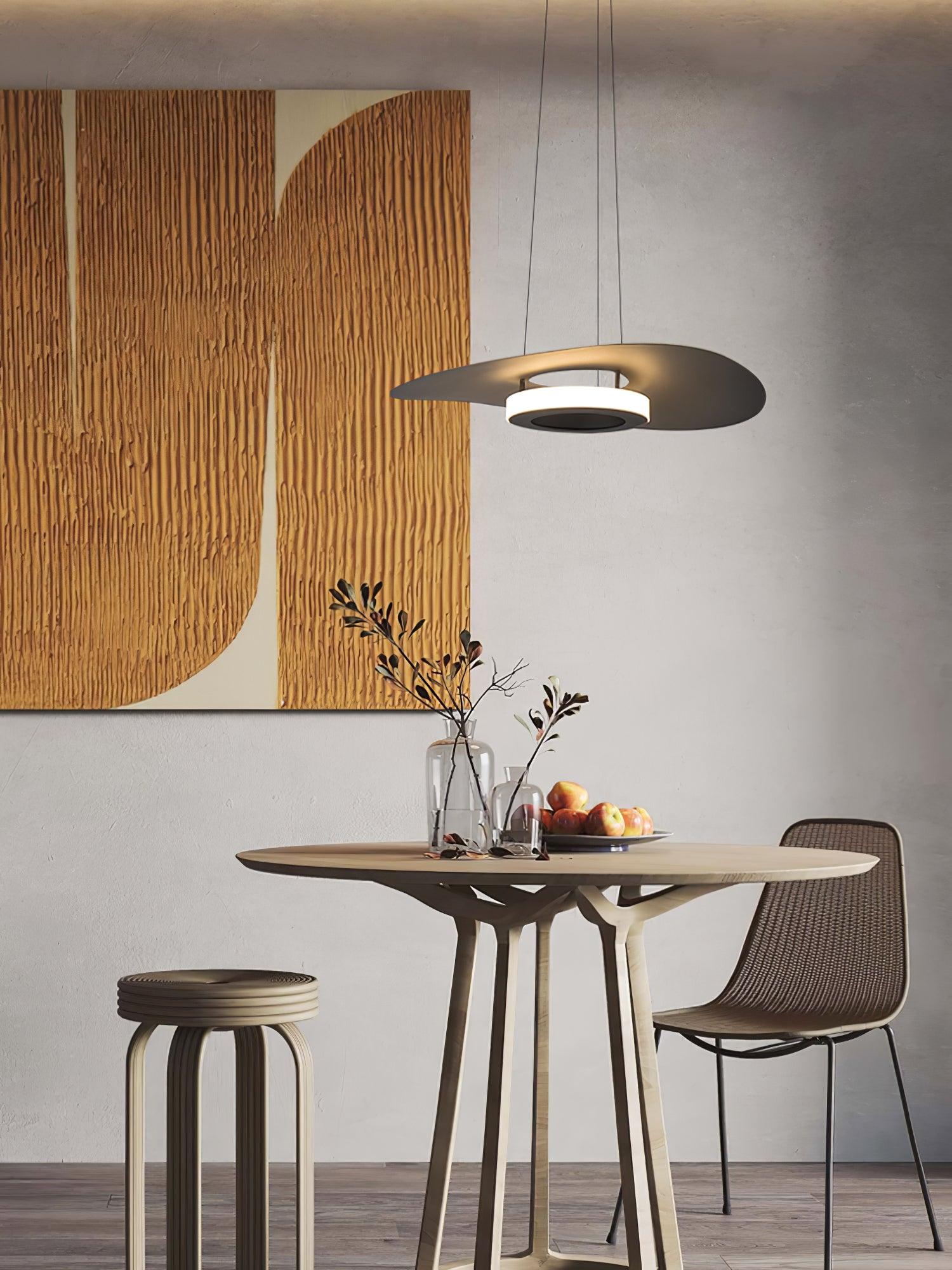 Wide view of dark disc light over round table with apples and branch vases beside wicker chair and stool