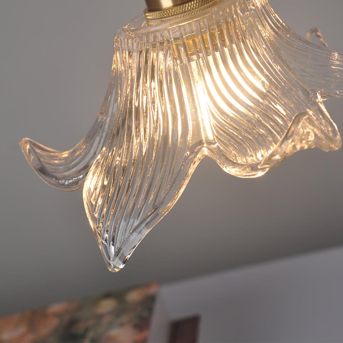 Close-up of illuminated clear glass ribs and a curling pointed petal beneath a knurled brass-toned collar.