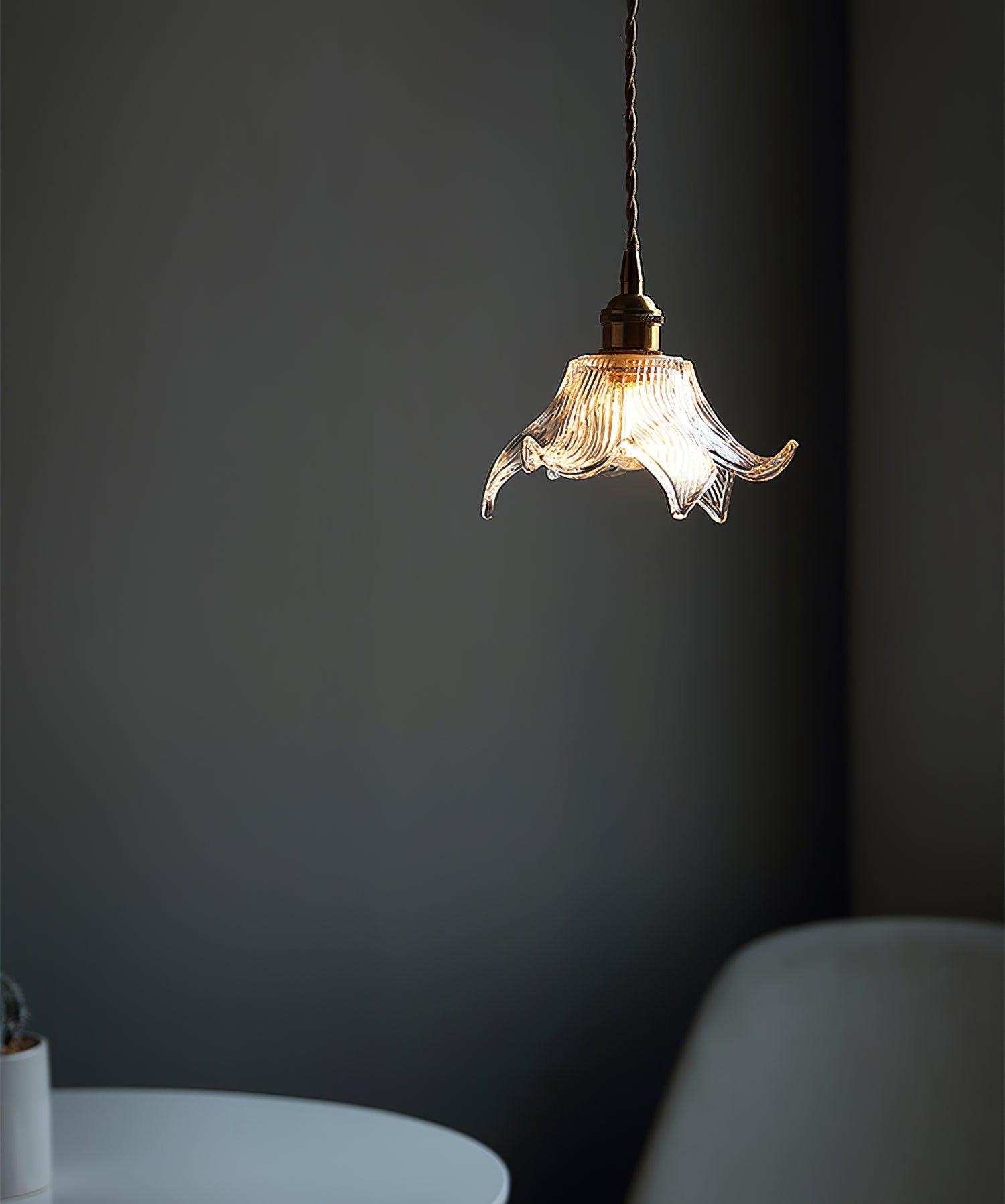 Single illuminated clear flower shade above a white table and pale upholstered chair against a dark grey wall.