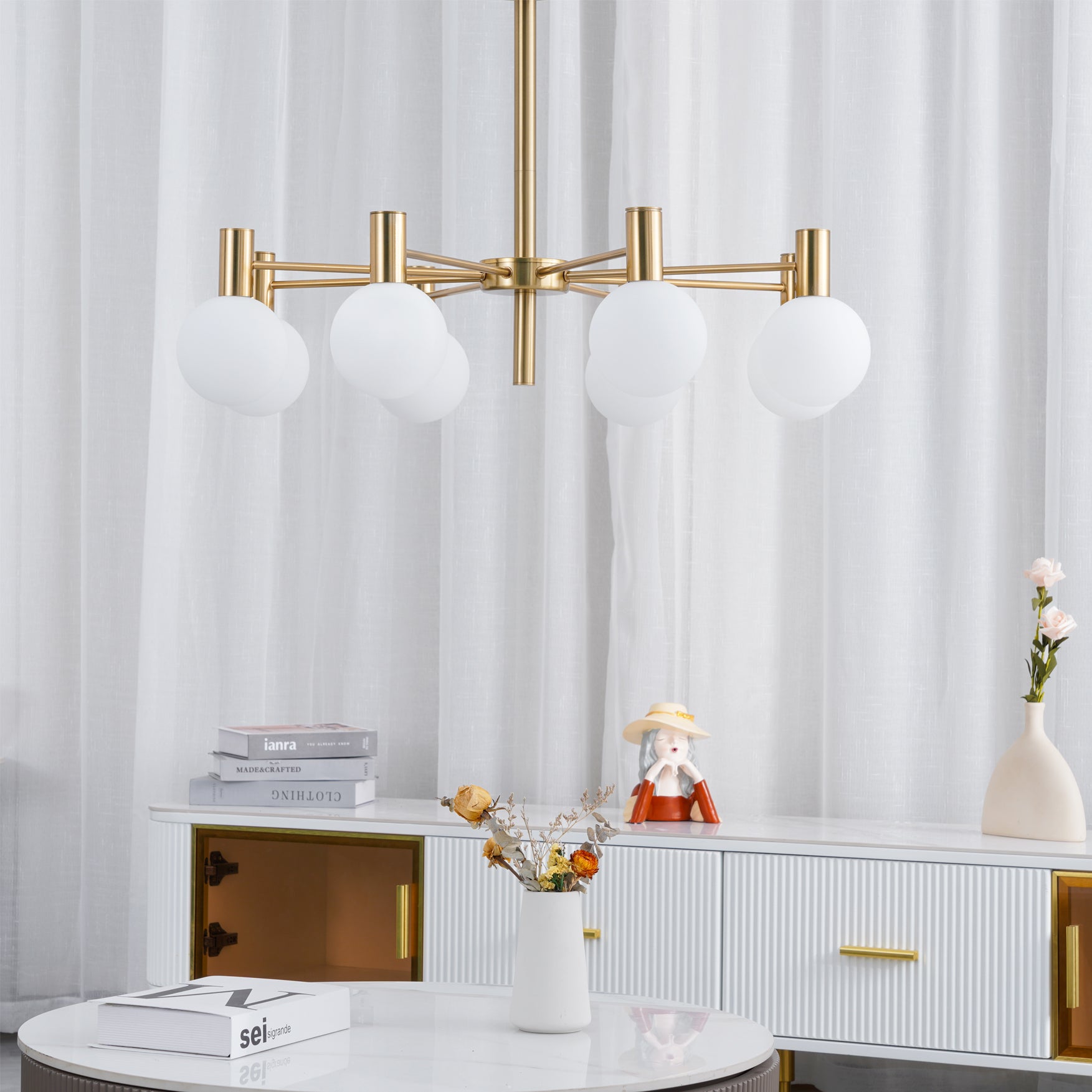 Unlit white-globe chandelier above a ribbed white cabinet and round table, with a gold-tone compartment and flowers.