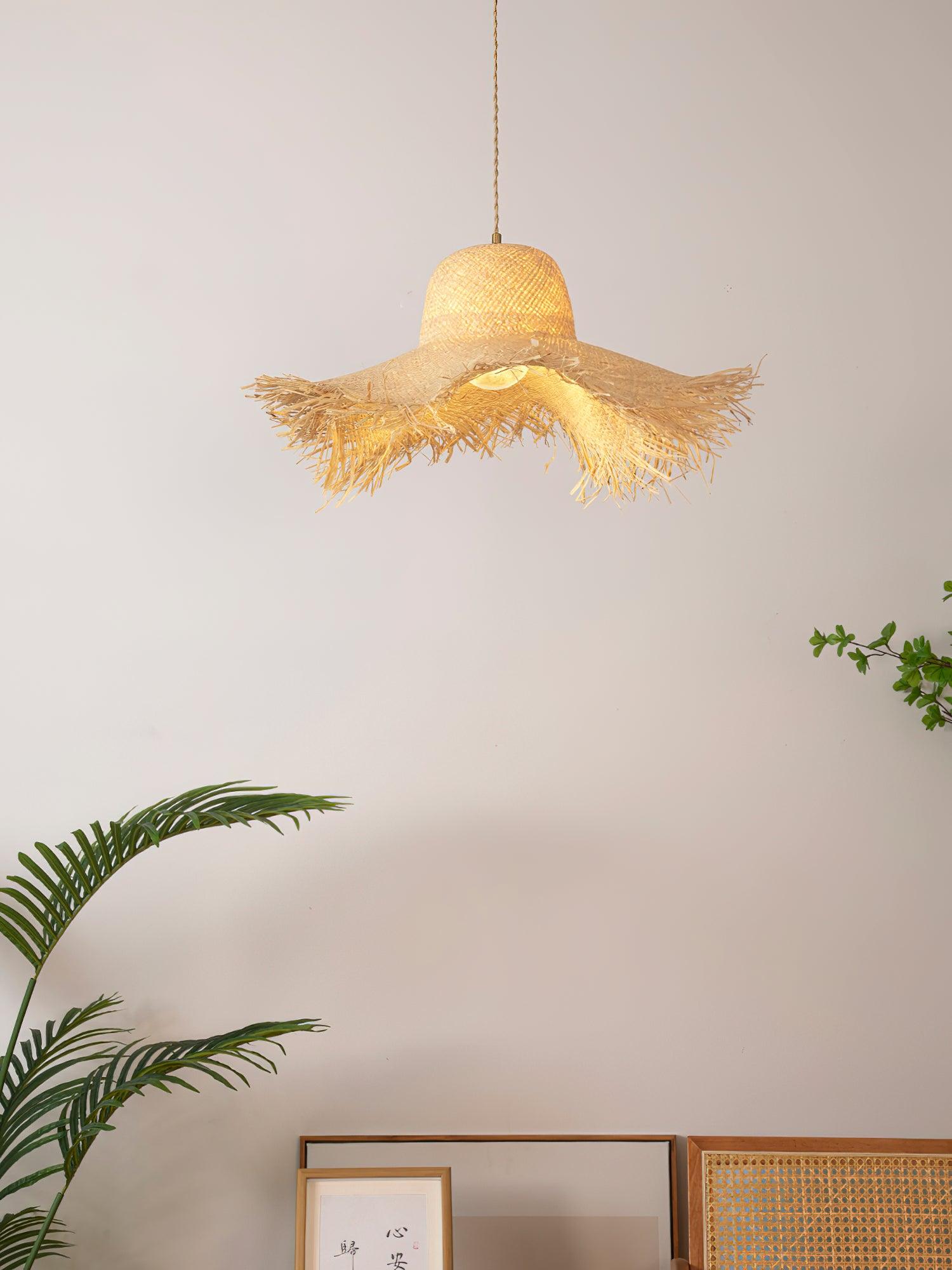 Lit fringed hat pendant with round bulb visible under the brim above leaning artwork and cane furniture