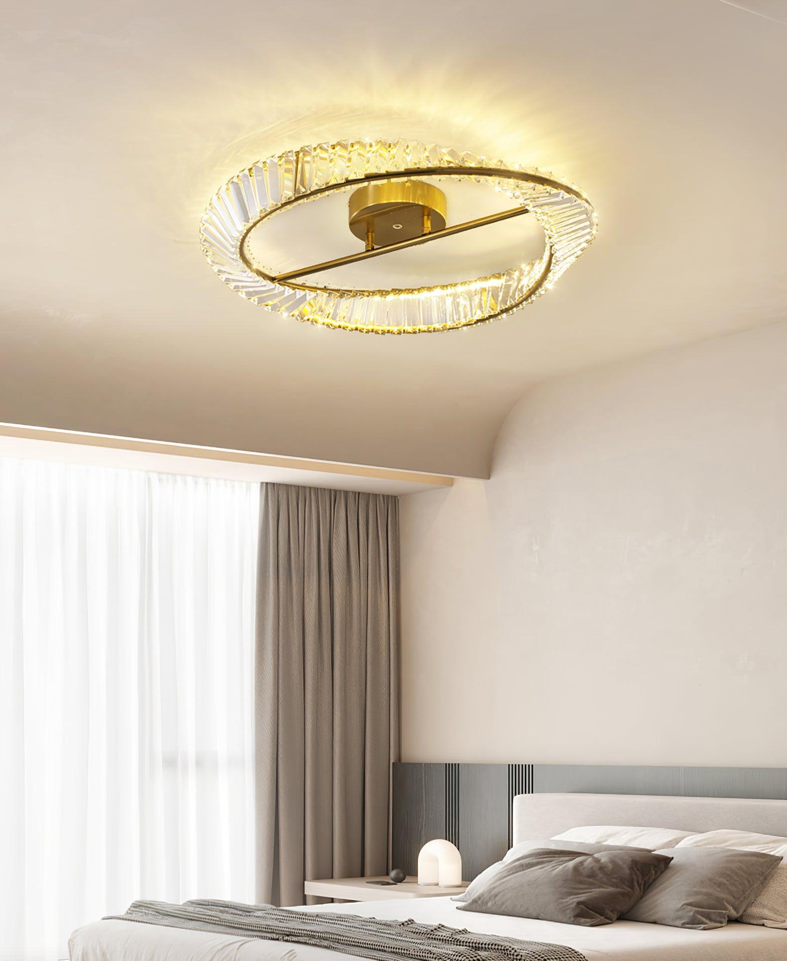 Gold-tone ring ceiling light above a bed with grey pillows and sheer window curtains