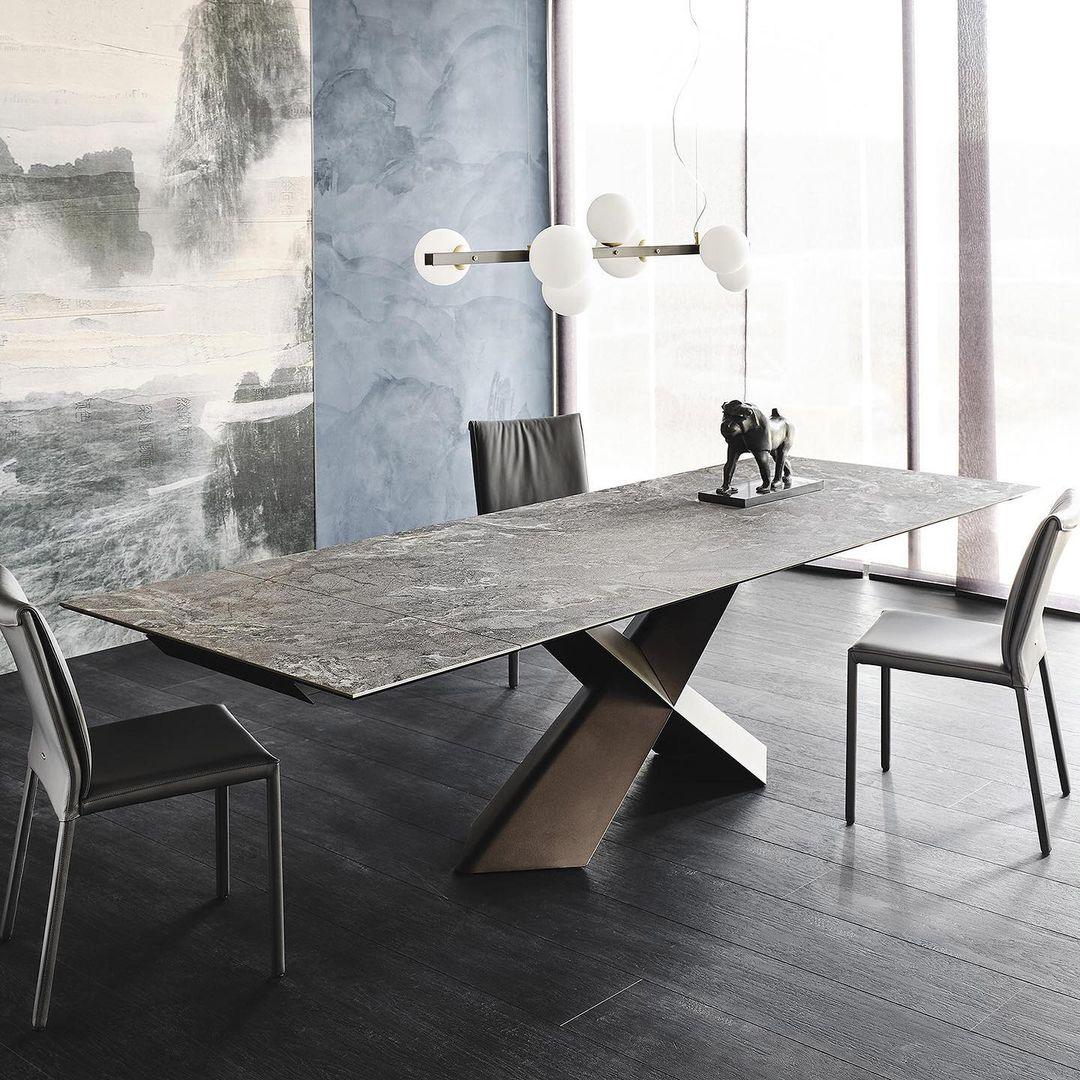 Globe pendant above grey veined table and black dog sculpture, beside dark chairs, bright curtain and blue wall with mural.