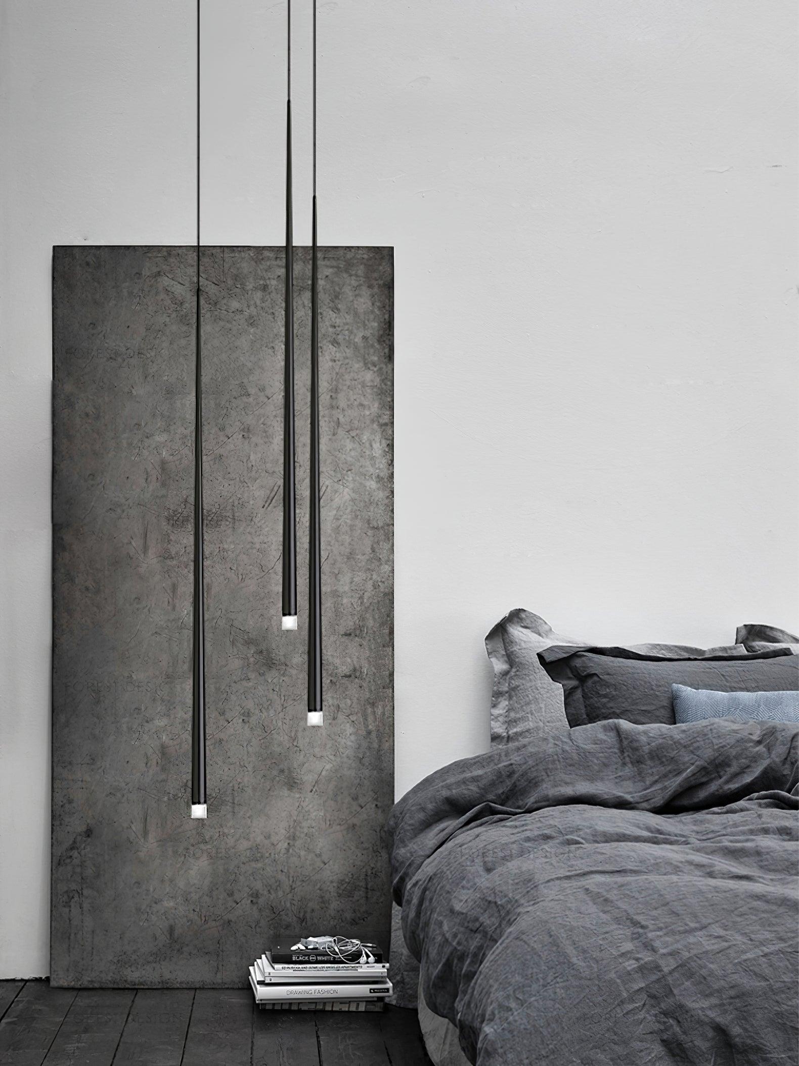 Three staggered black tube pendants beside a grey bed and tall stone-look panel