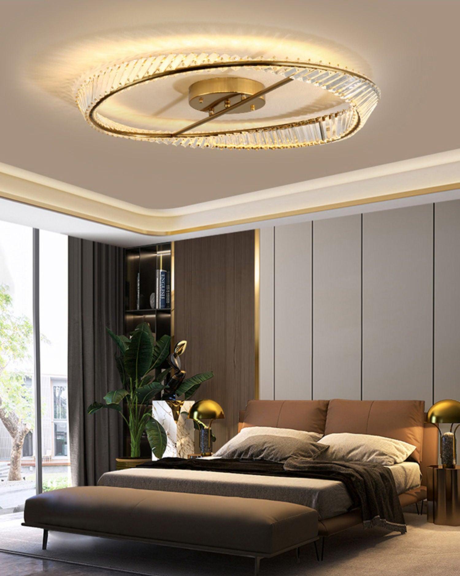Gold-tone glass ring light above a tan headboard and grey bench with separate bedside table lamps